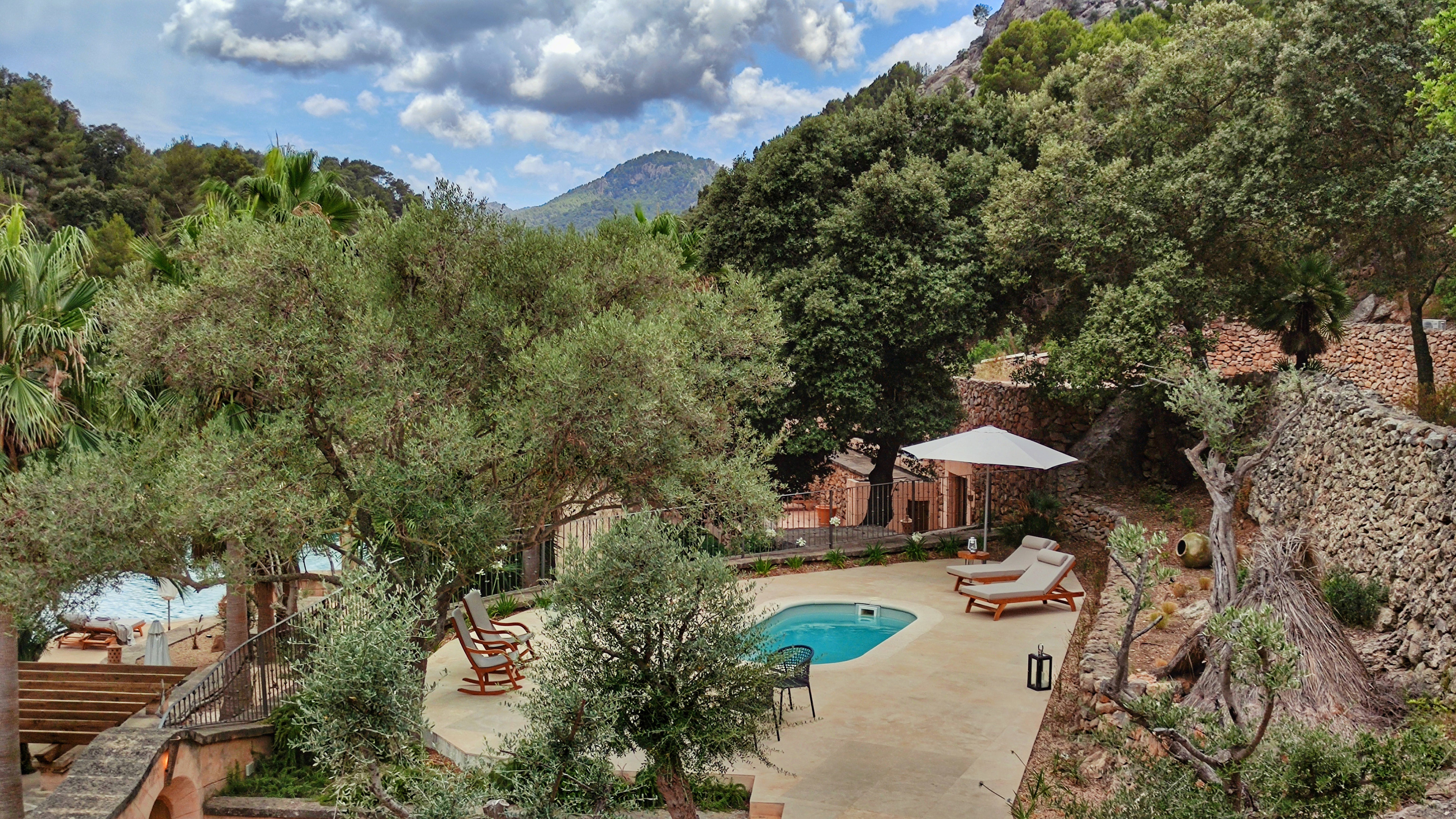 Private pool area with sun loungers, olive trees, and mountain backdrop.