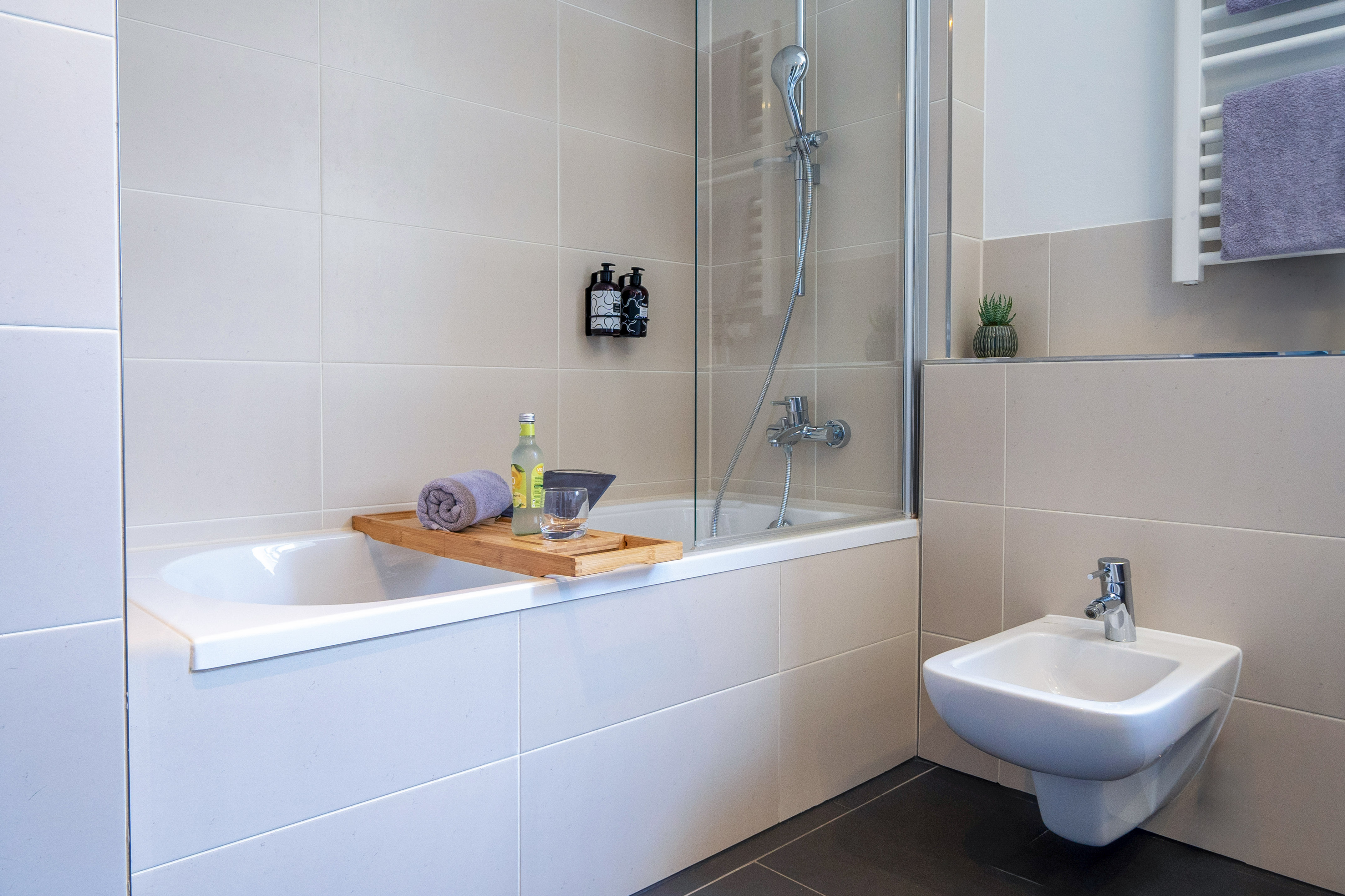 Modern tiled bathroom with bathtub, shower, bidet, and bath caddy.