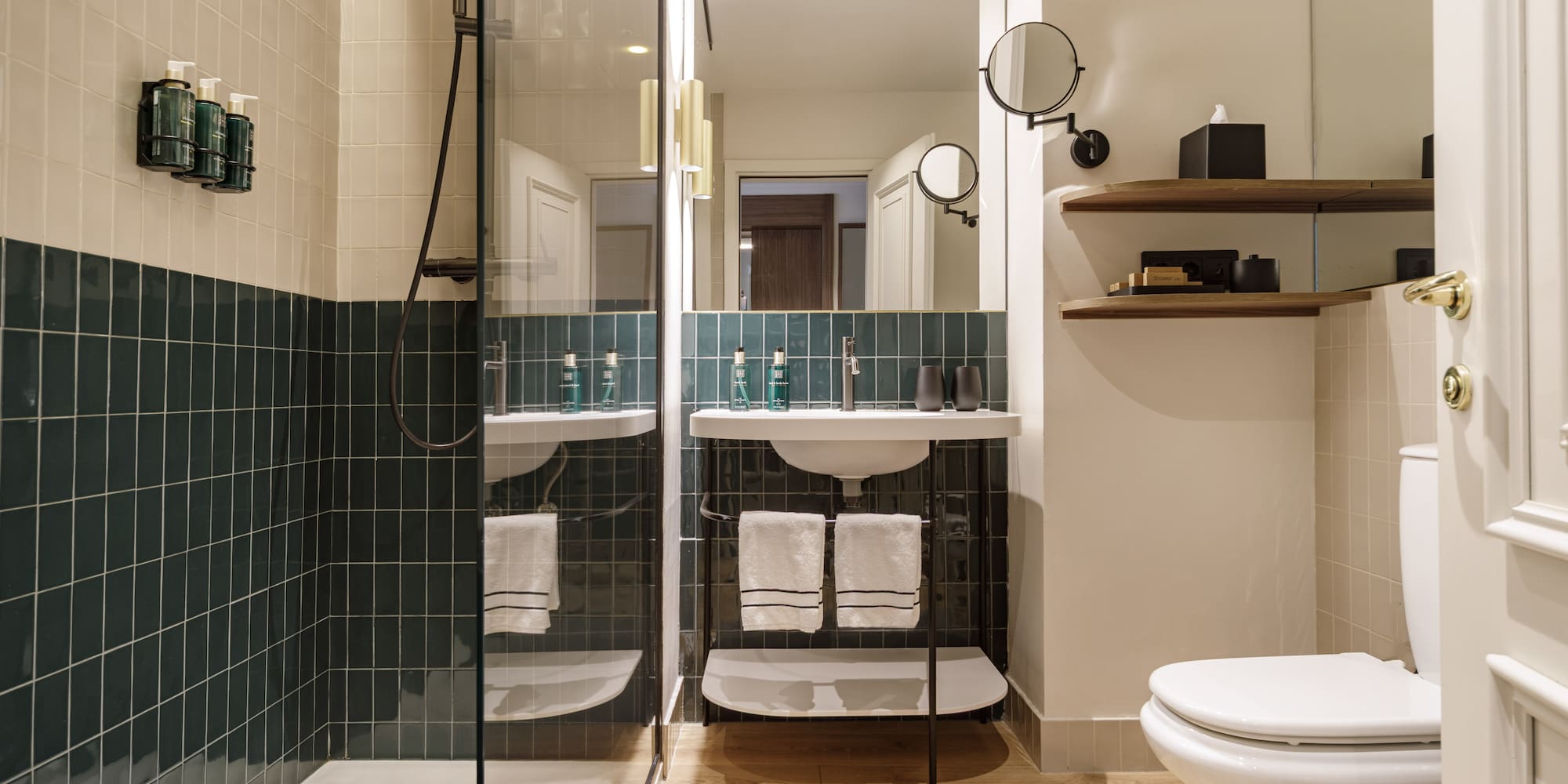 Contemporary hotel bathroom with green tiled shower, modern vanity, and toilet.