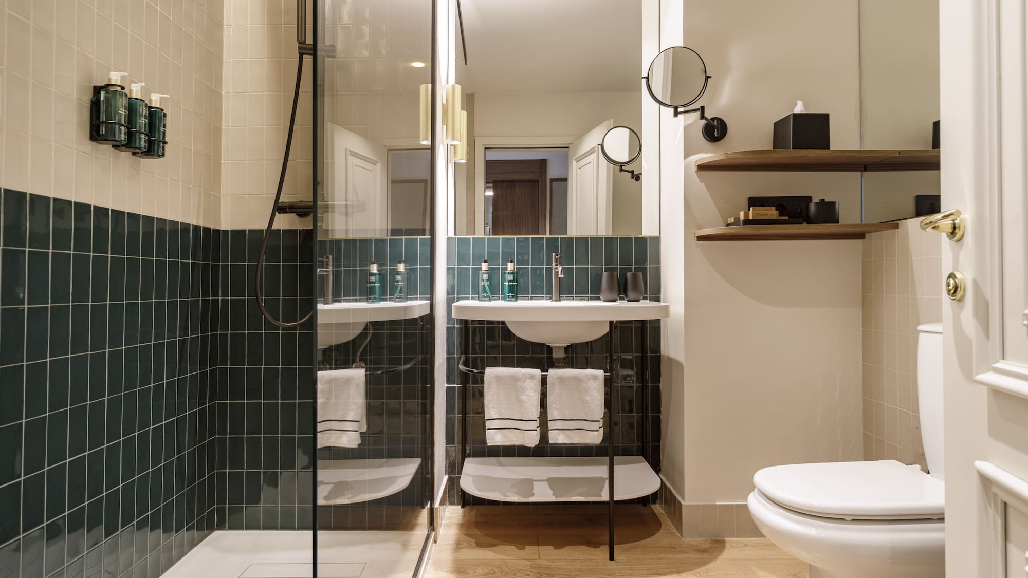 Contemporary hotel bathroom with green tiled shower, modern vanity, and toilet.