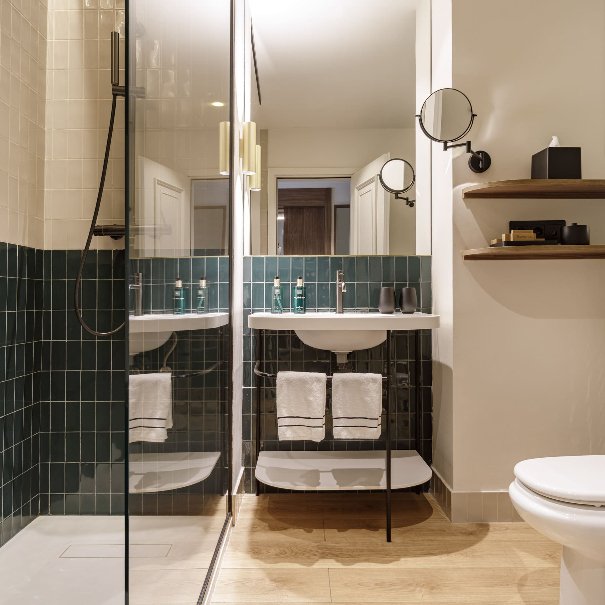 Contemporary hotel bathroom with green tiled shower, modern vanity, and toilet.
