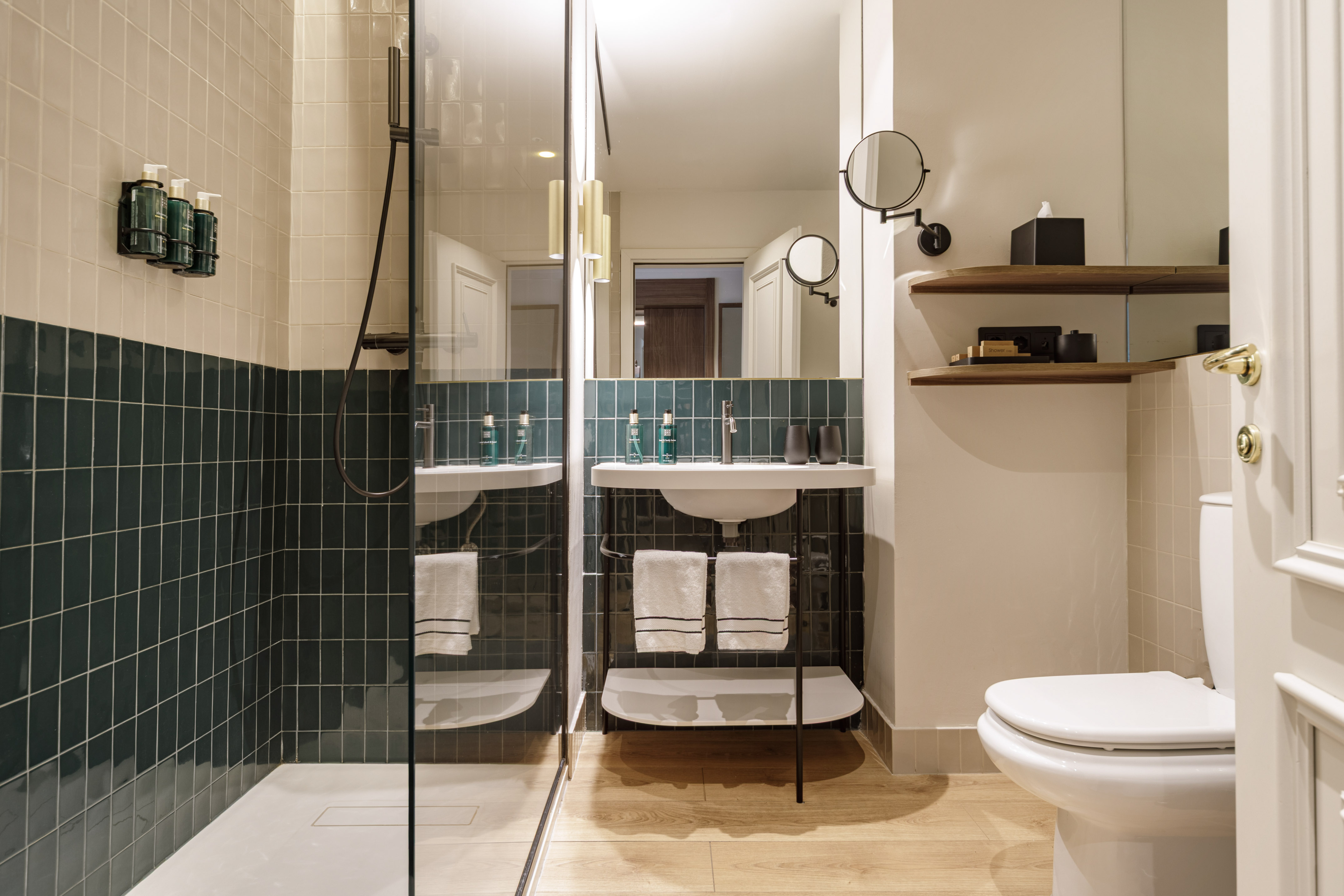 Contemporary hotel bathroom with green tiled shower, modern vanity, and toilet.