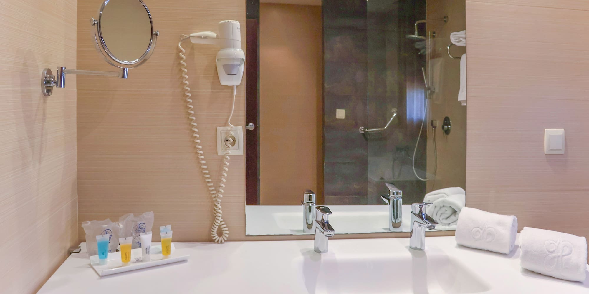 Hotel bathroom vanity with sink, mirror, hairdryer, amenities, and white towels.