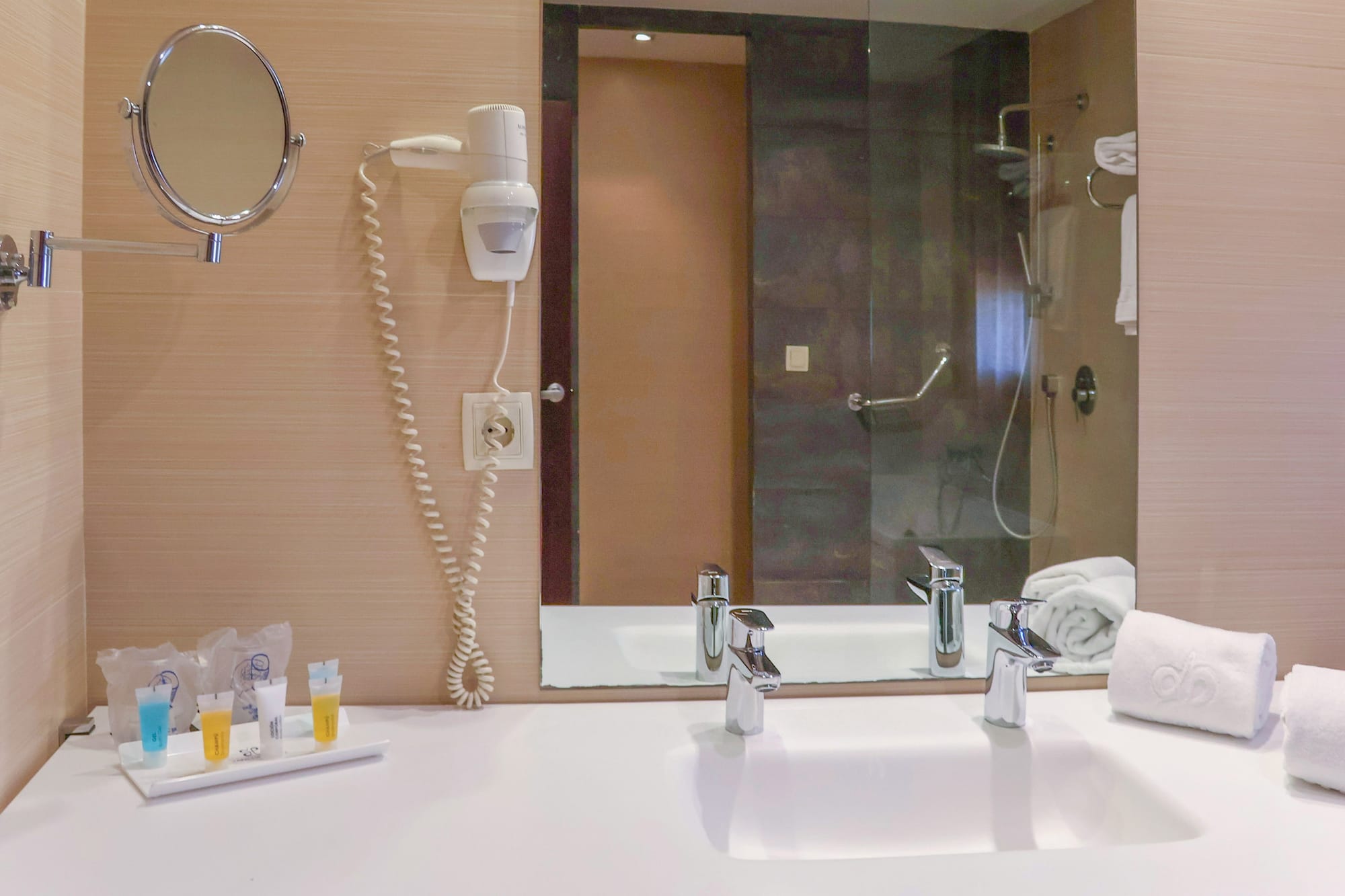 Hotel bathroom vanity with sink, mirror, hairdryer, amenities, and white towels.