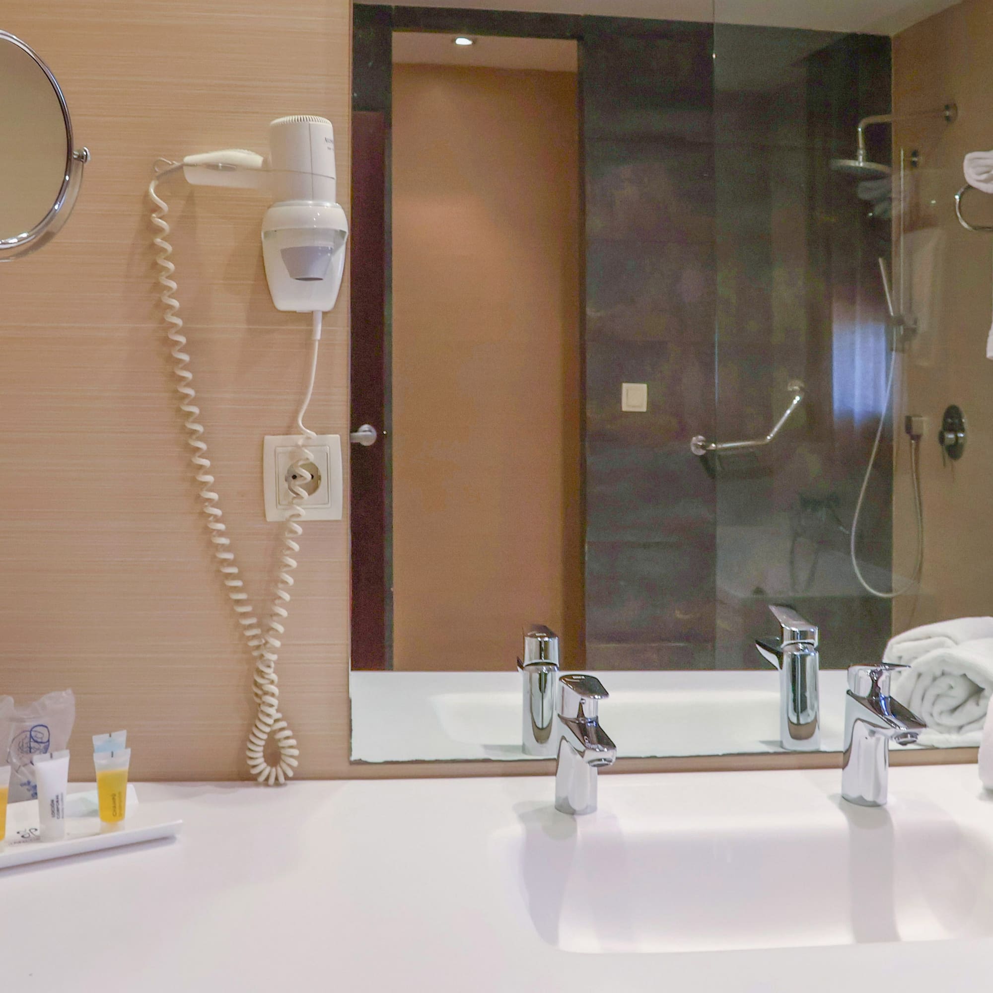 Hotel bathroom vanity with sink, mirror, hairdryer, amenities, and white towels.