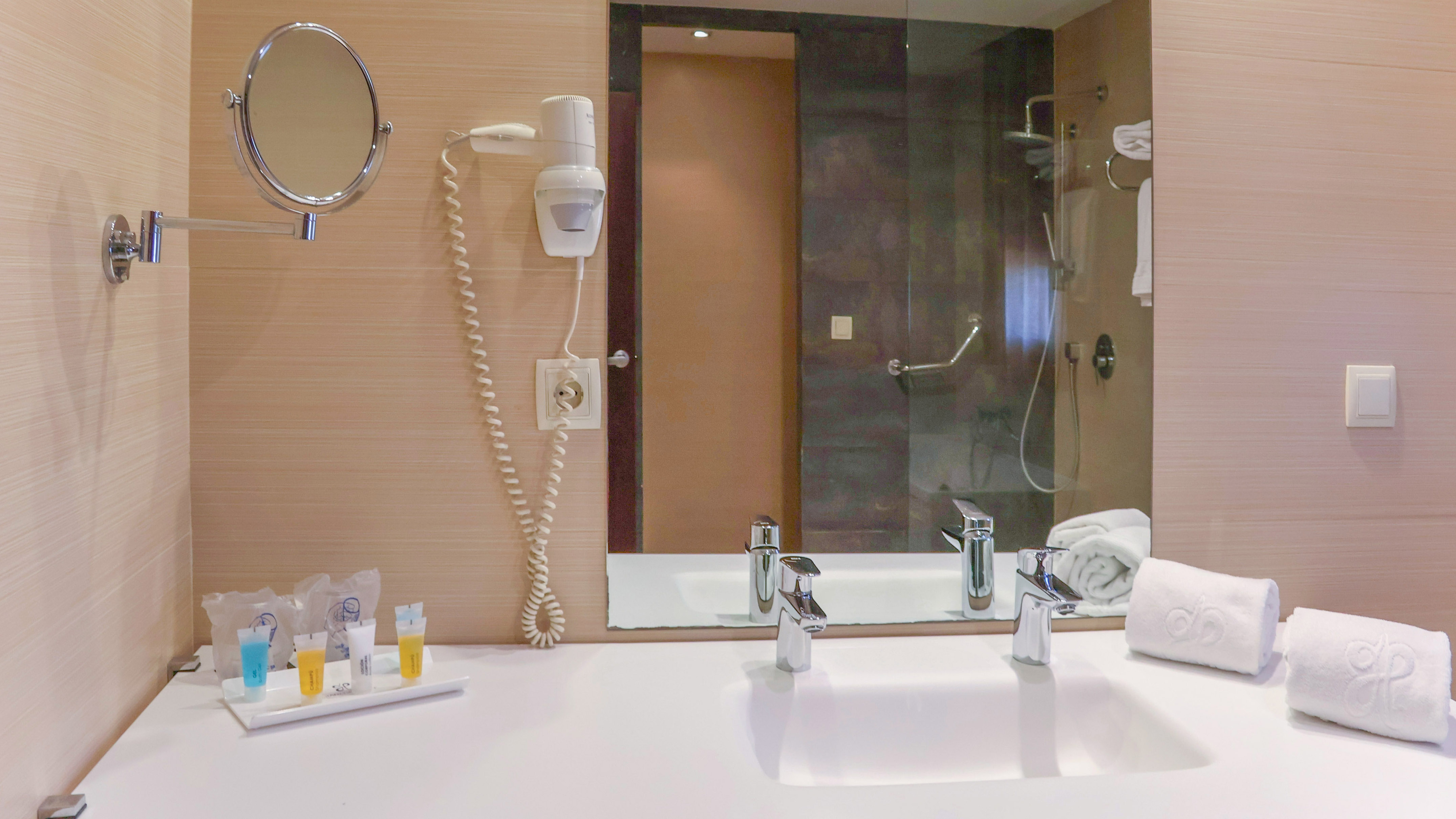 Hotel bathroom vanity with sink, mirror, hairdryer, amenities, and white towels.