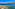 Malta: Bahía azul con pueblo costero, muelle y playa rocosa con bote.
