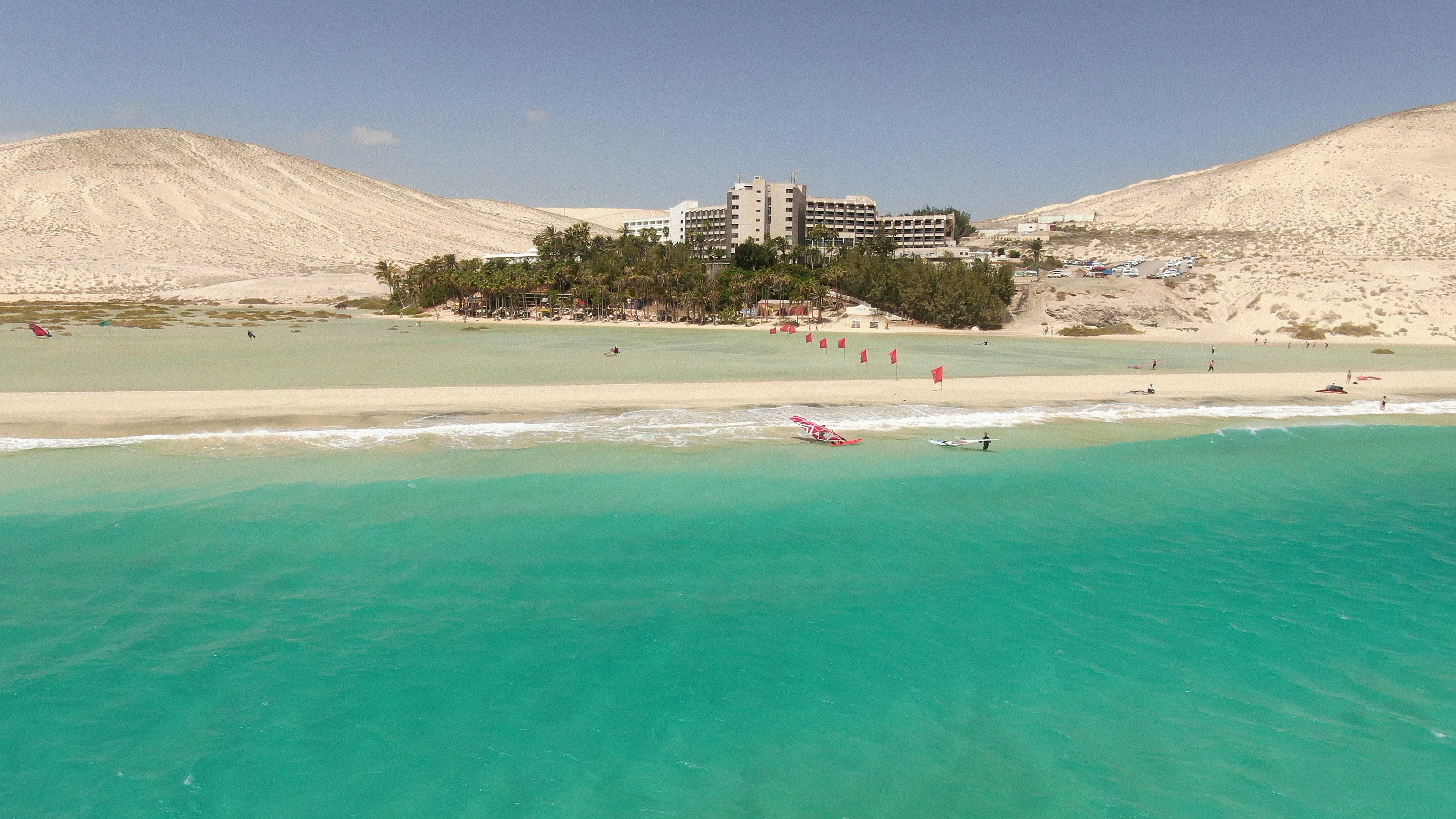 Windsurfing on turquoise lagoon near sandy beach, resort, and desert dunes.