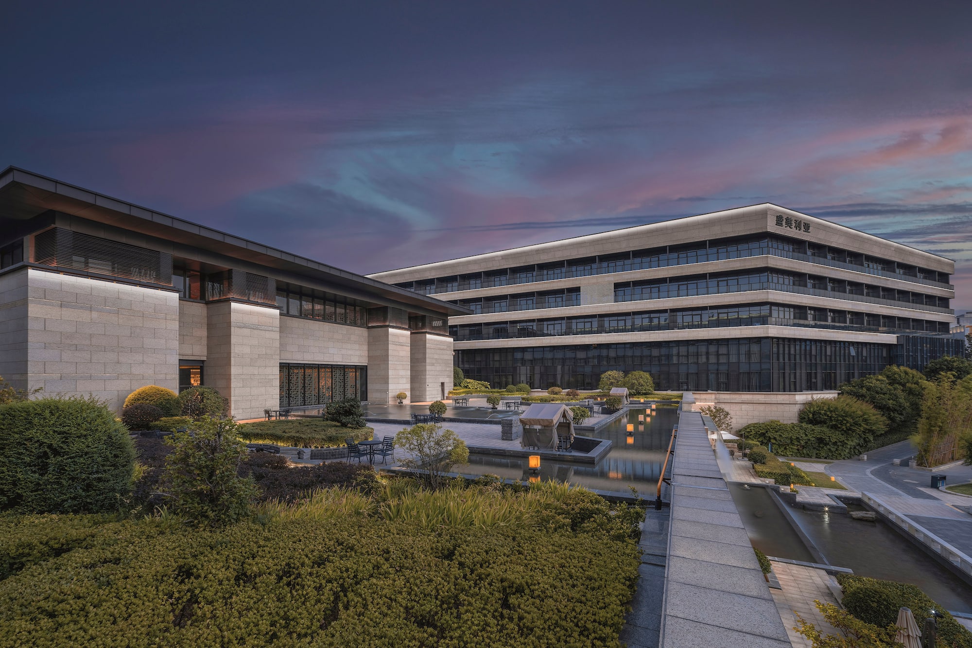 Modern hotel complex, landscaped grounds, reflecting pond, vibrant dusk.