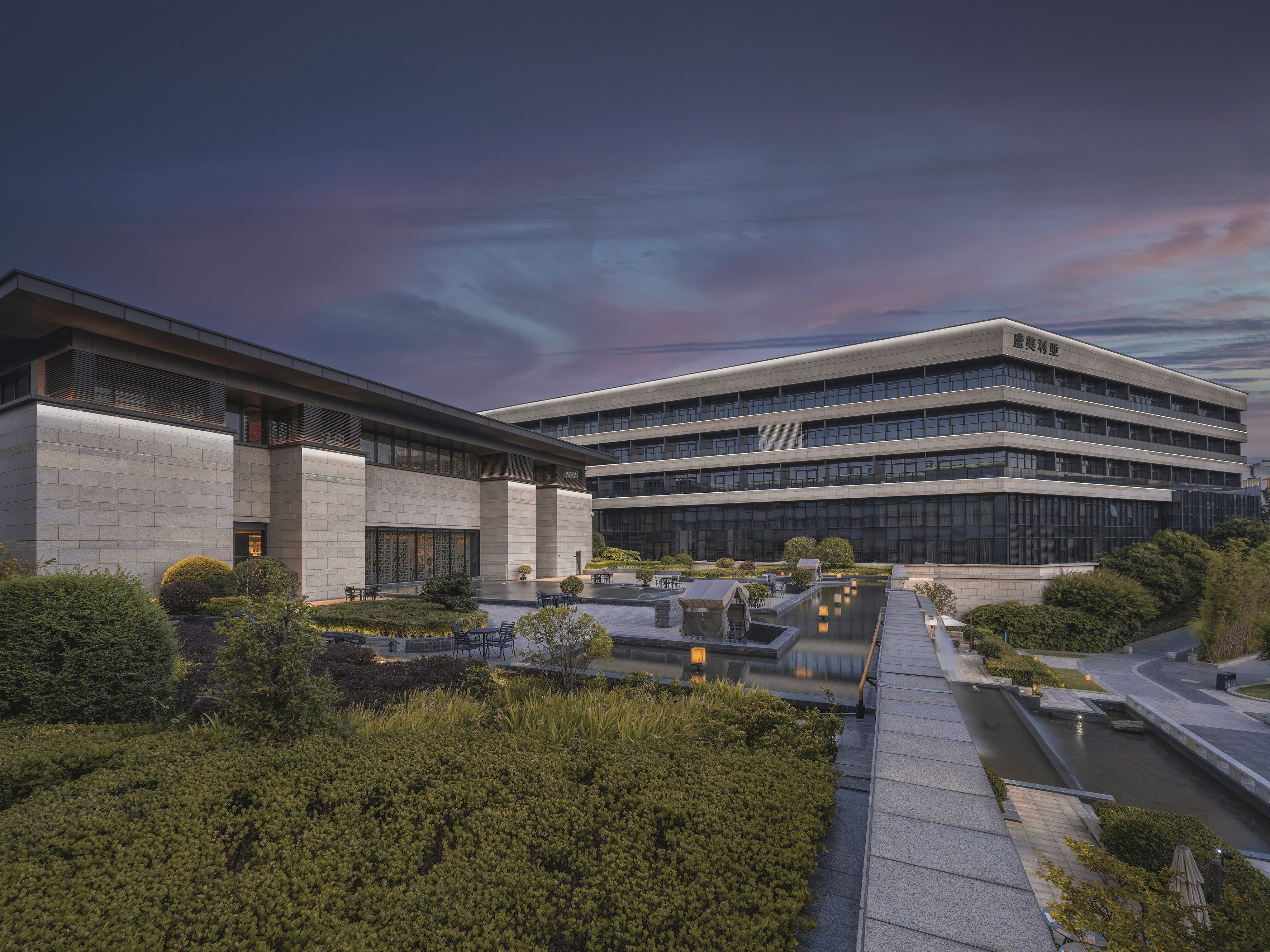 Modern hotel complex, landscaped grounds, reflecting pond, vibrant dusk.