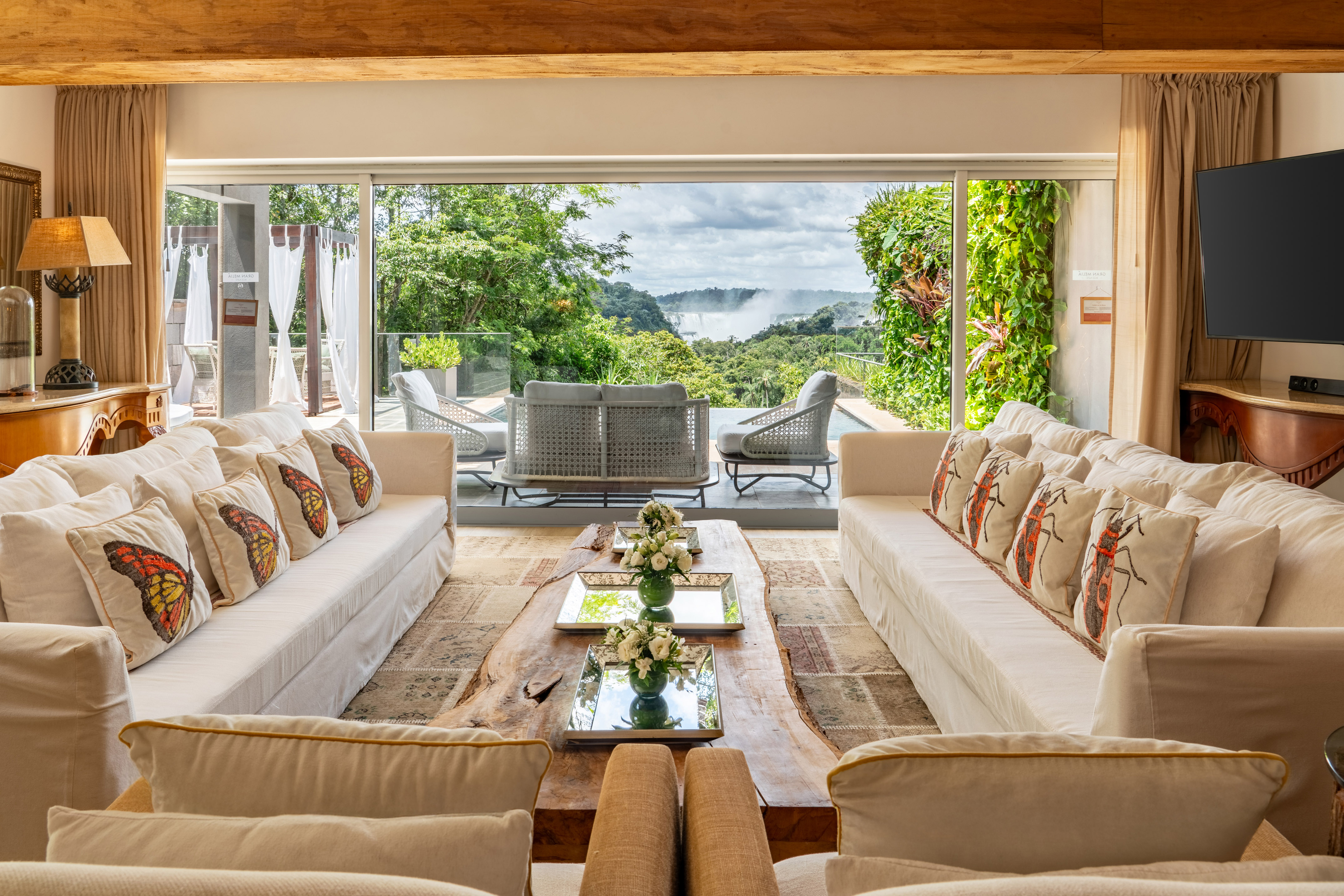 Luxury living room with white sofas and panoramic waterfall view.