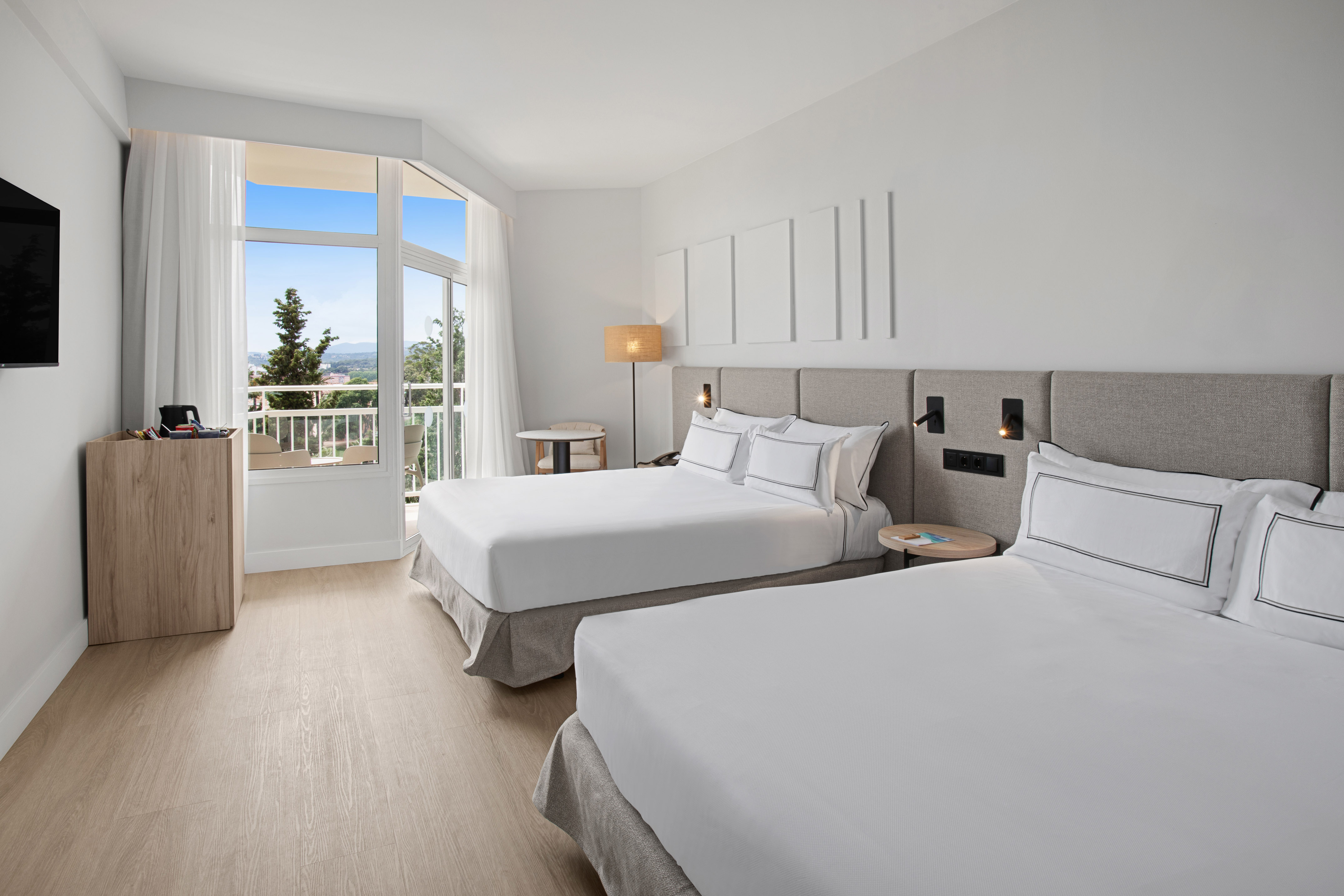 Modern hotel room with two beds and balcony overlooking a scenic view.