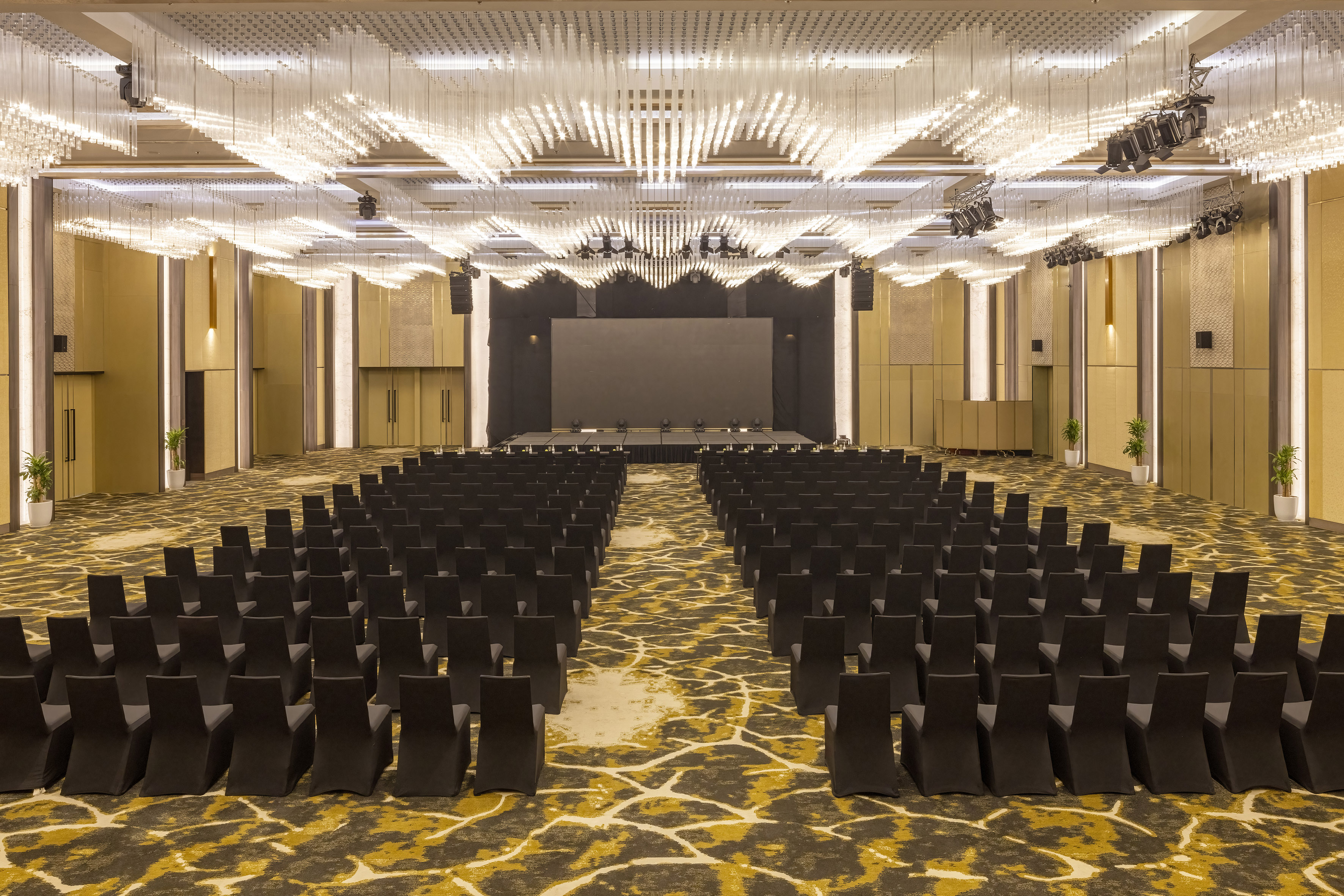 Modern conference room setup: stage, screen, black chairs, elegant lighting.