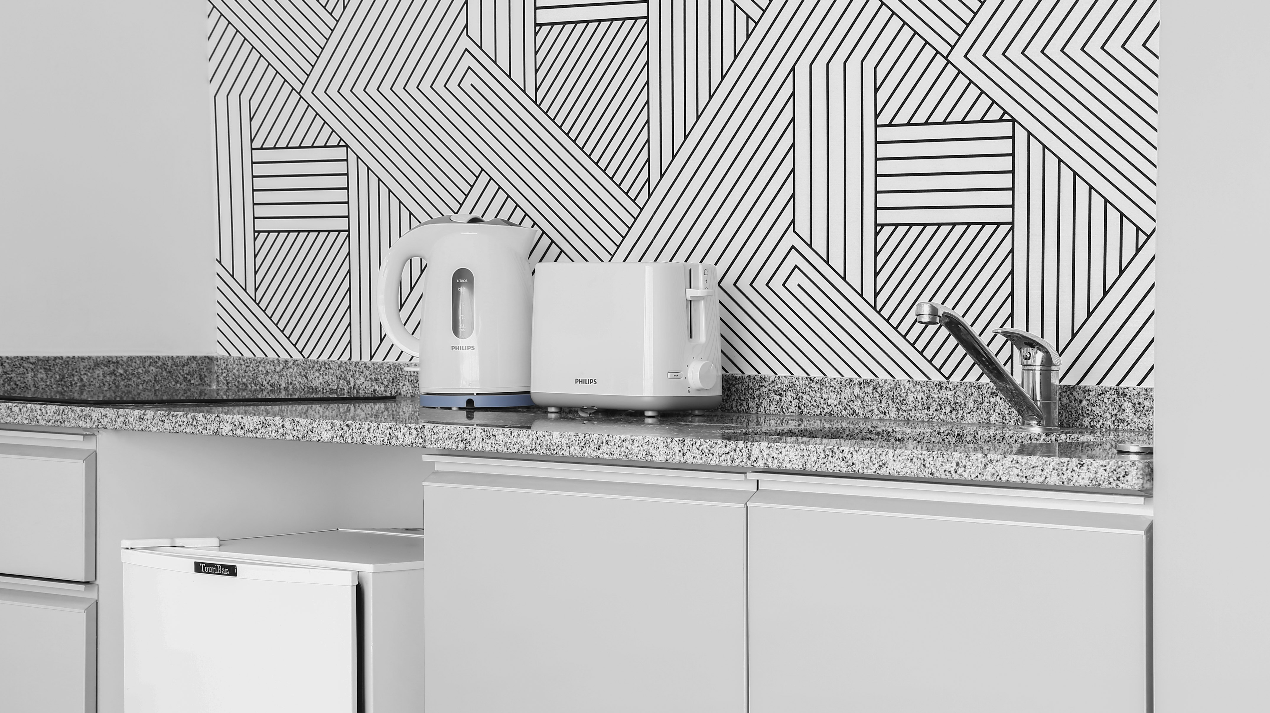 Modern kitchenette with white kettle, toaster, granite counter, geometric backsplash.