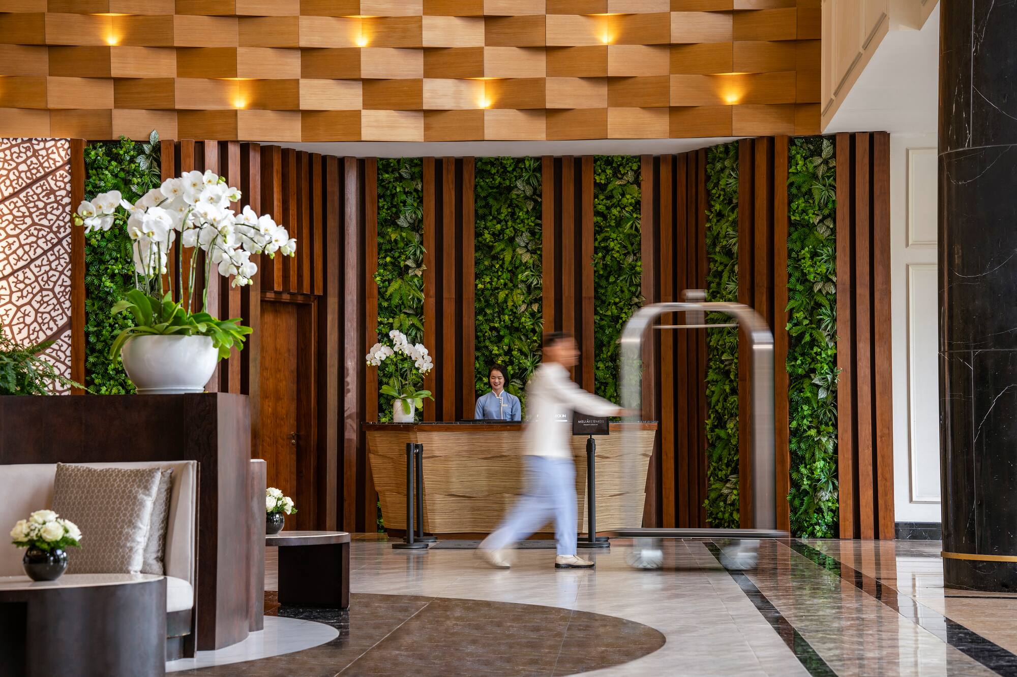 Hotel reception desk with green wall, white orchids, and a bellhop.