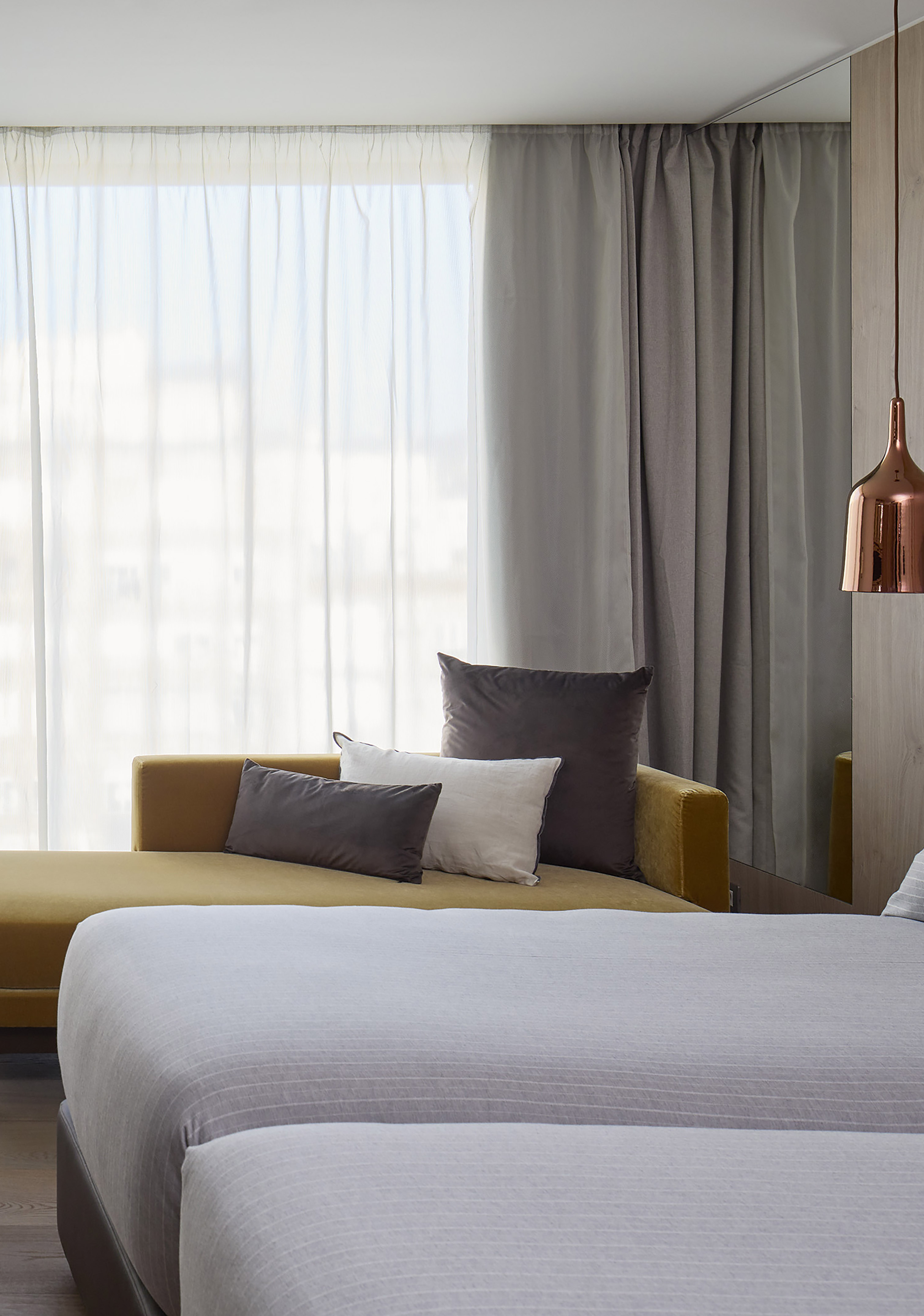Modern bedroom with yellow chaise lounge, sheer curtains, and copper pendant light.