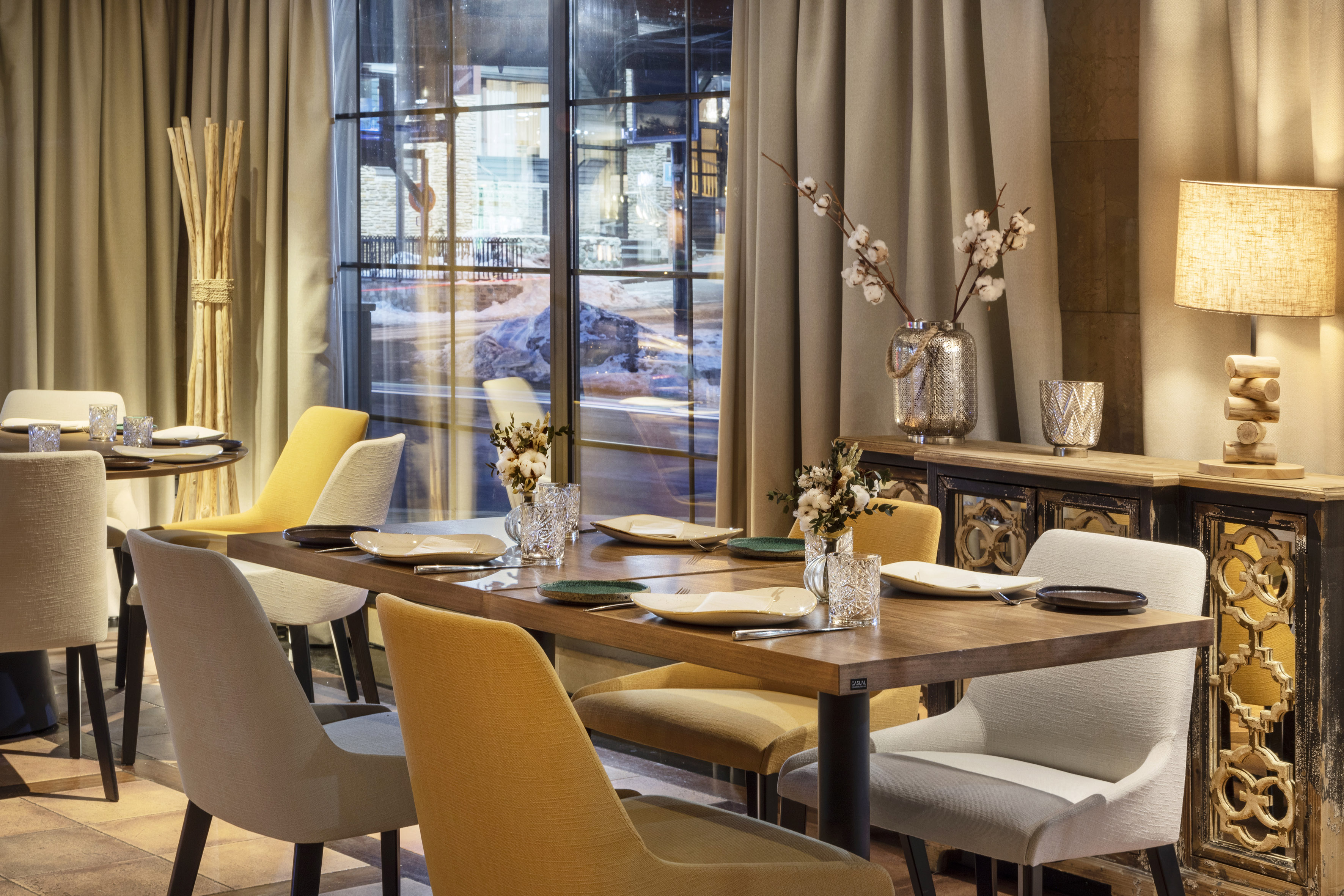Modern restaurant dining room with set wooden tables and mustard chairs.