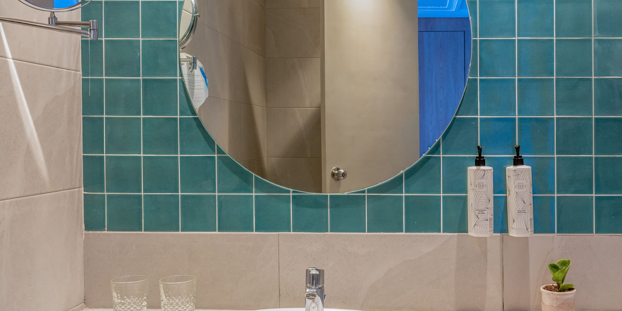 Hotel bathroom with marble vanity, white sink, round mirror, and teal wall tiles.