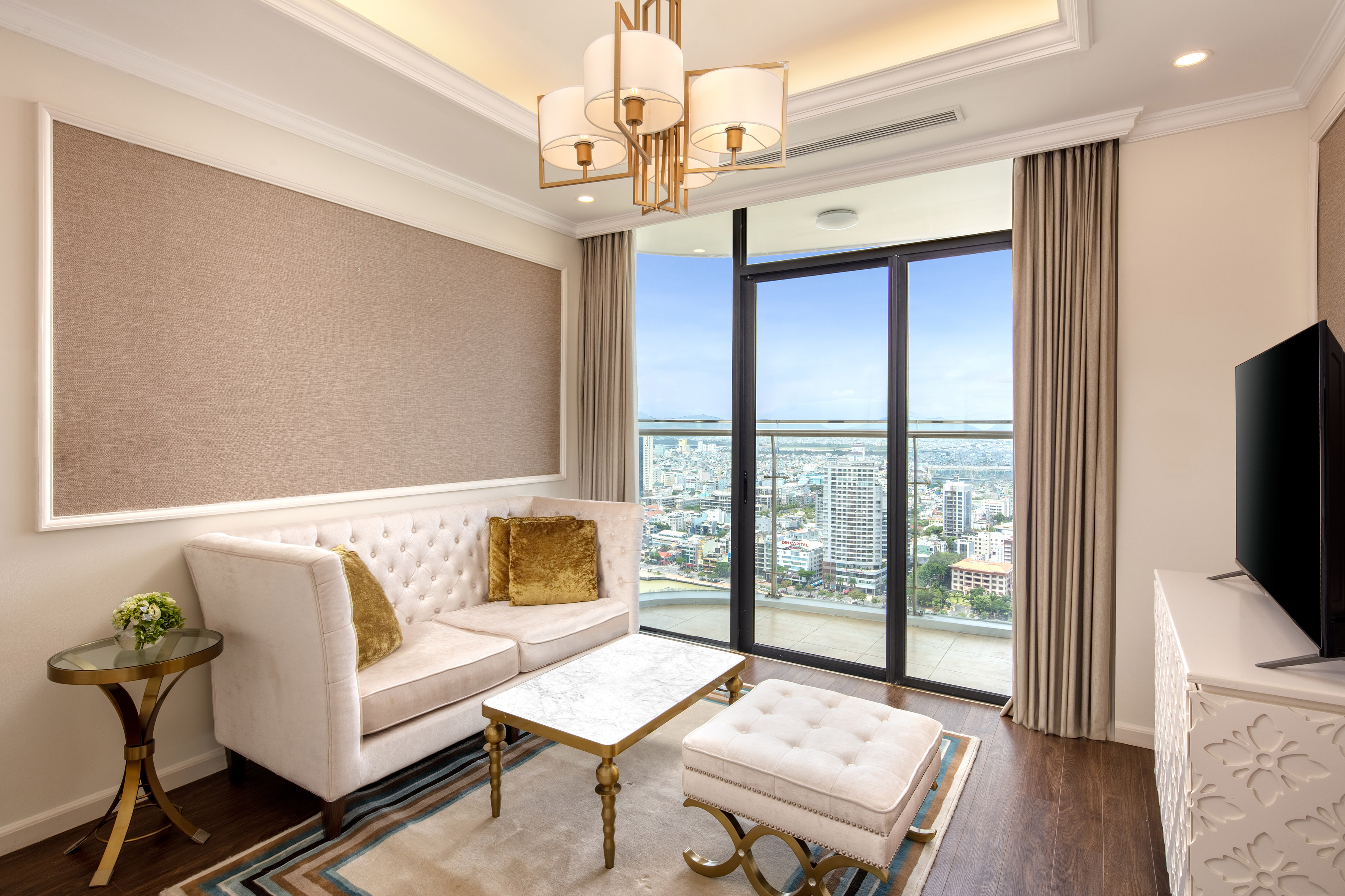 Modern living room with city view, tufted sofa, marble table, and gold chandelier.