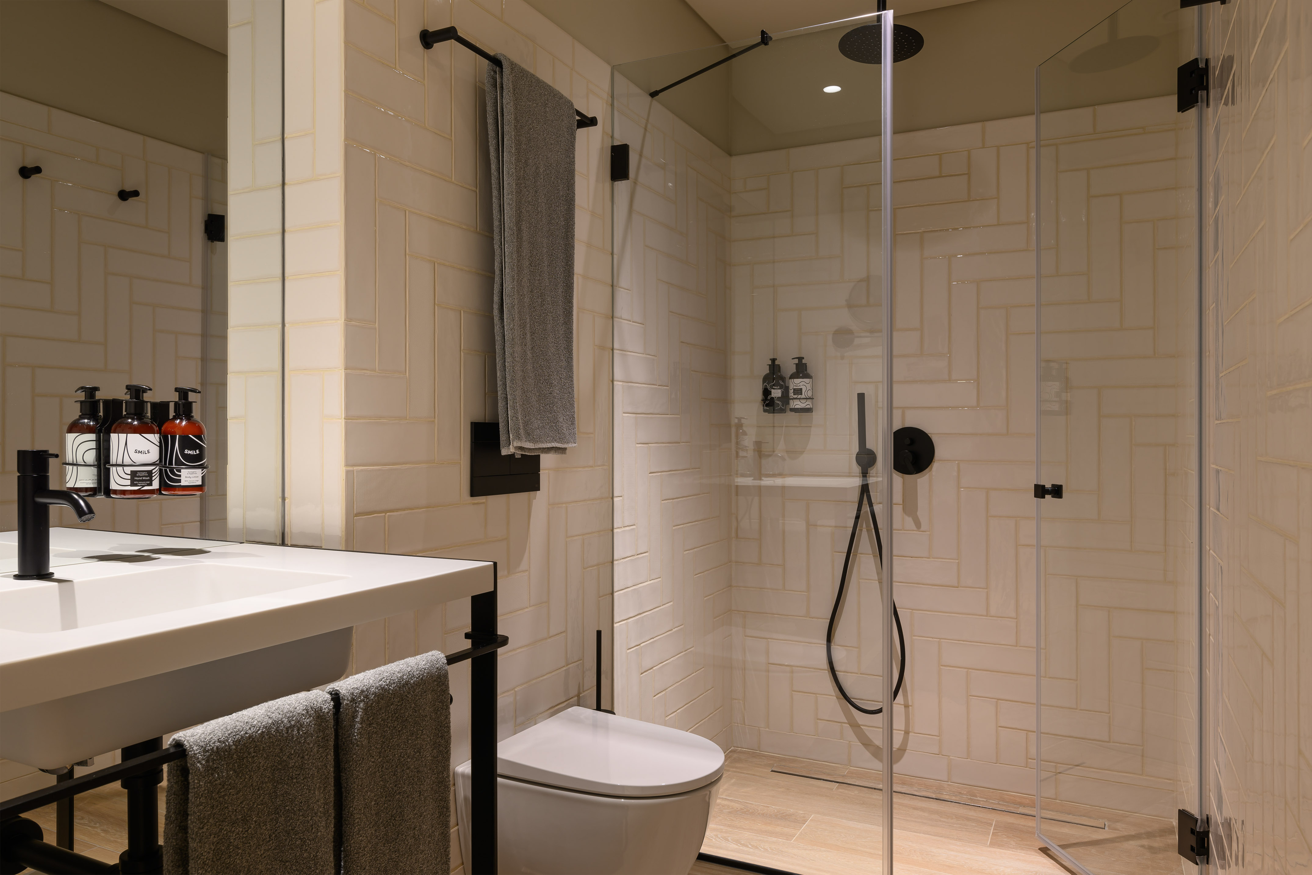 Modern bathroom with white herringbone tiles, black fixtures, and glass walk-in shower.