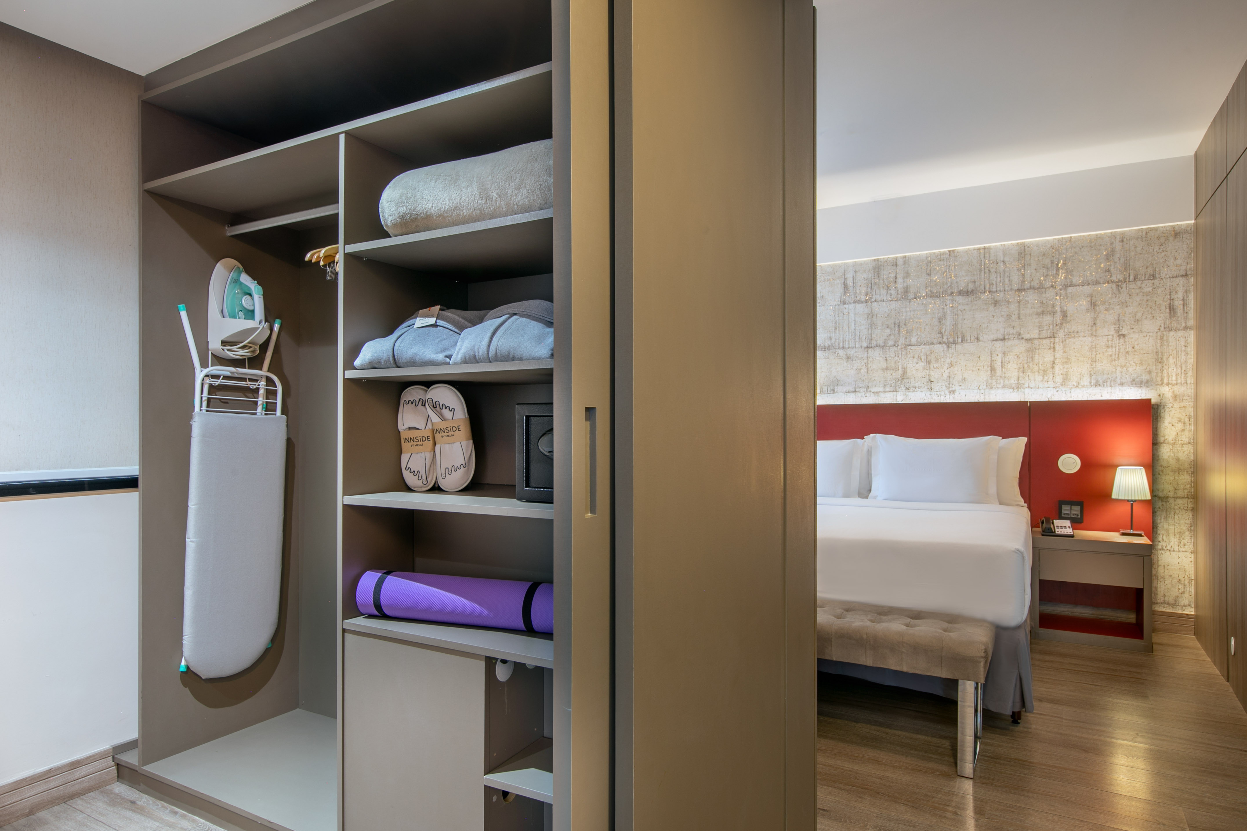 Hotel room with open closet featuring ironing board, yoga mat, bathrobes, and bed.