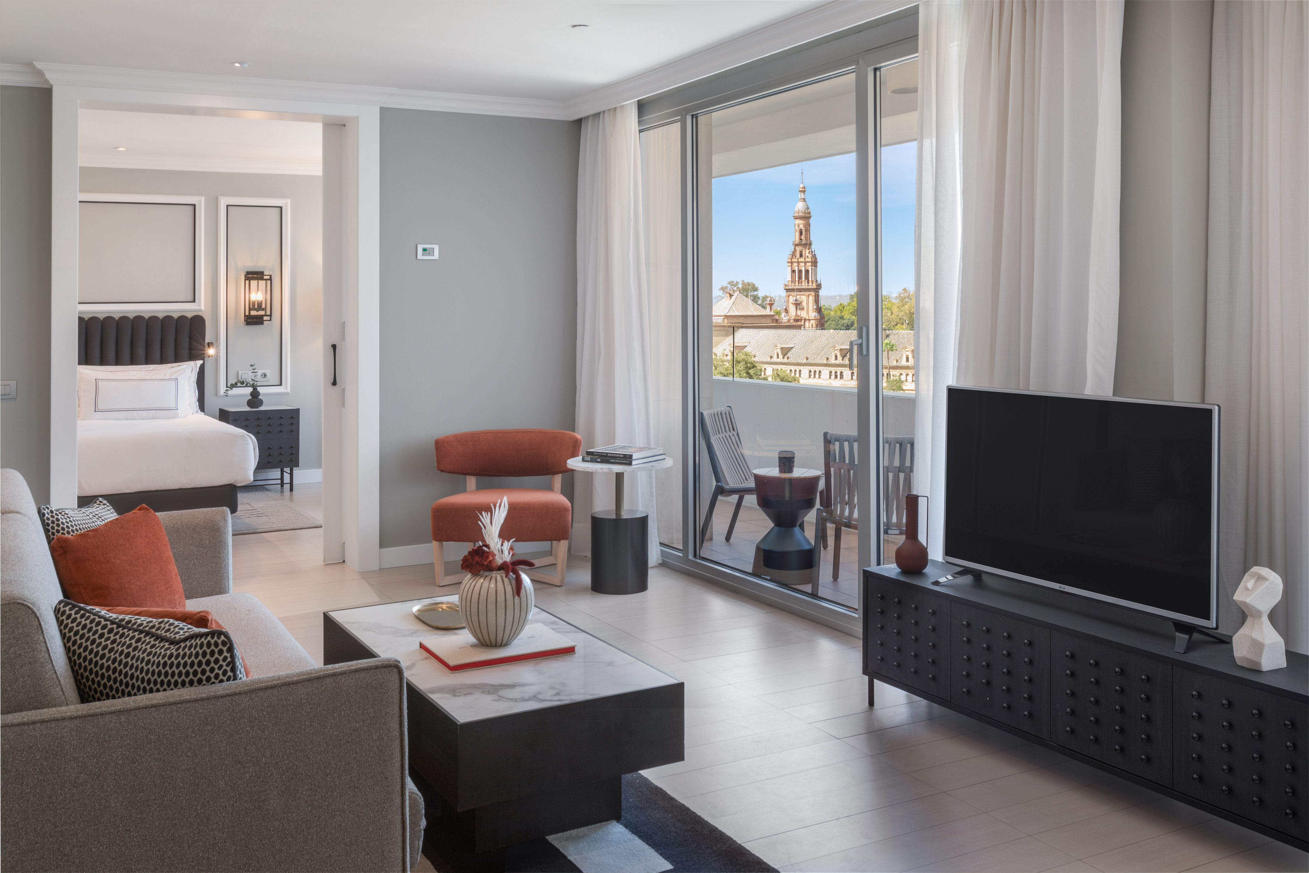 Modern hotel suite living room with balcony overlooking historic tower.