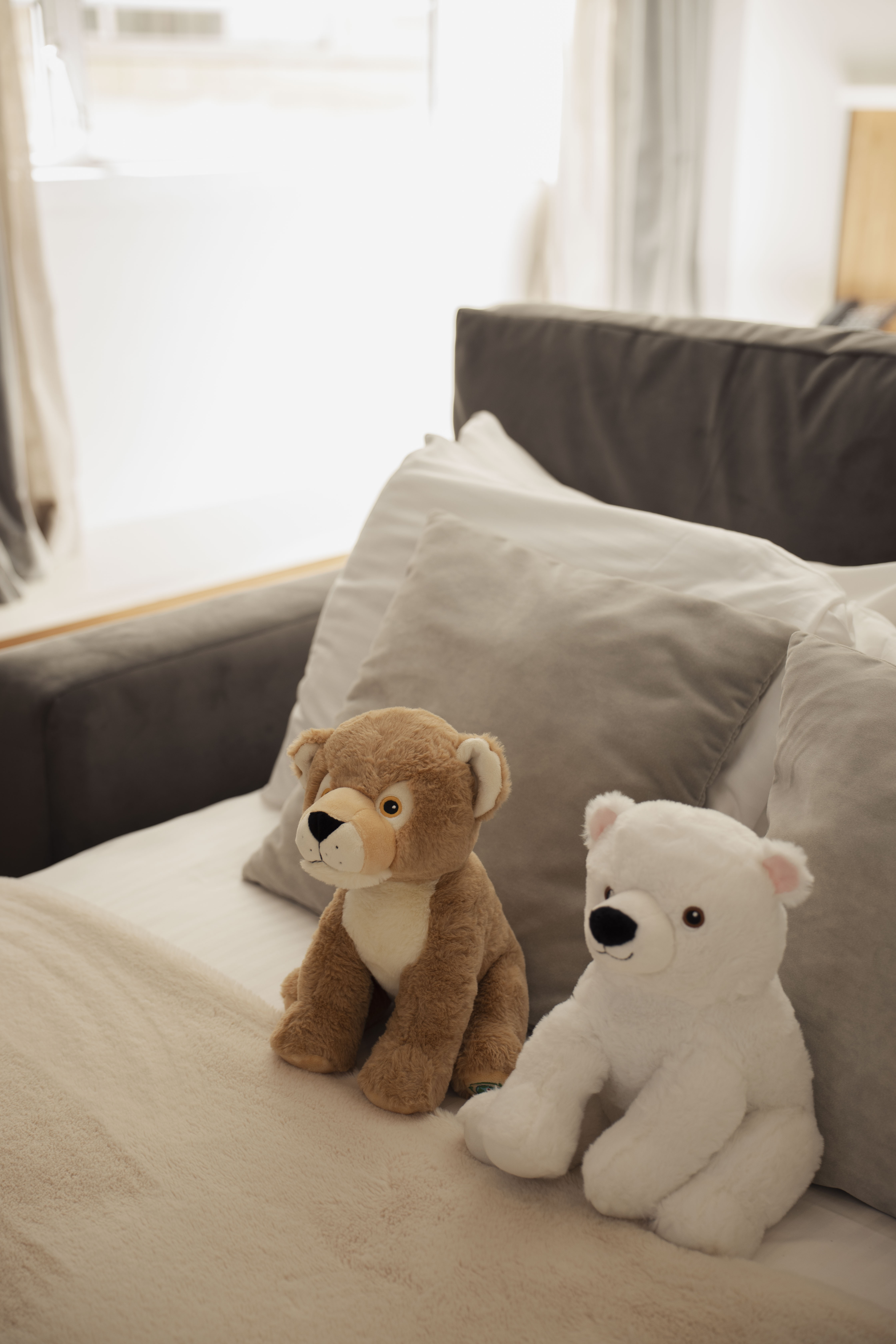 Brown lion and white polar bear plush toys on a cozy bed.