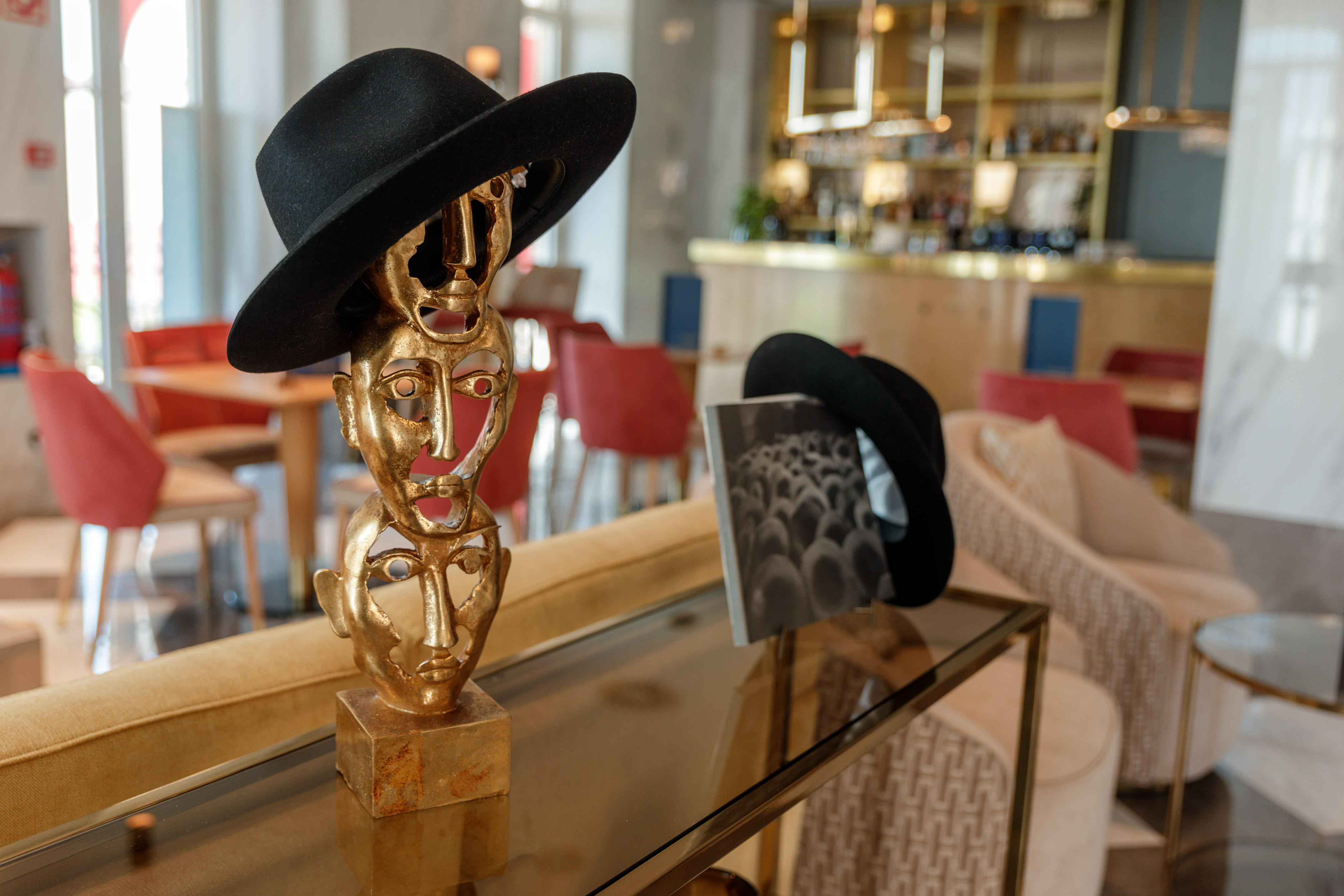 Golden stacked faces sculpture with black fedora, modern hotel lounge decor.