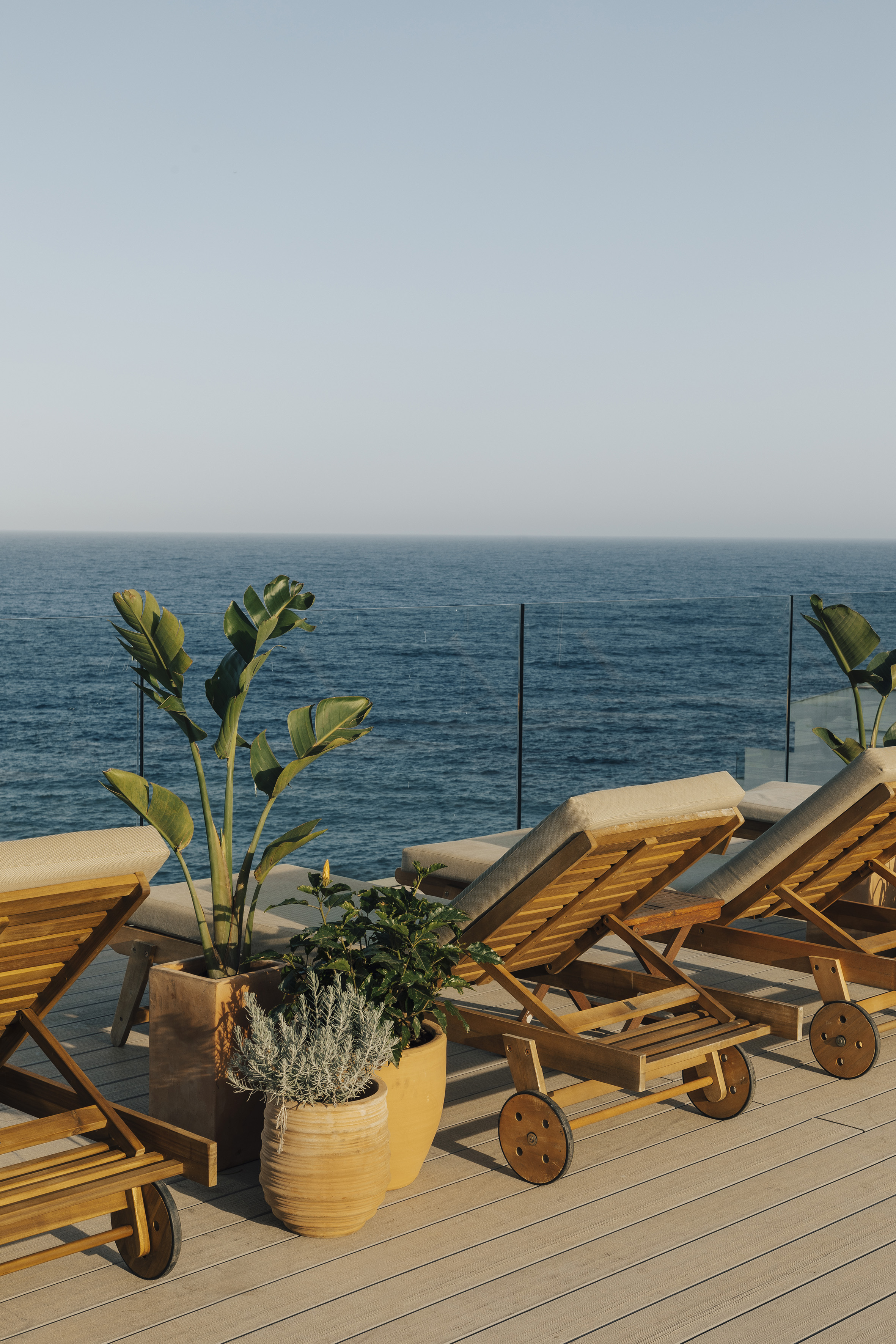 Ocean view terrace with wooden lounge chairs and potted plants.