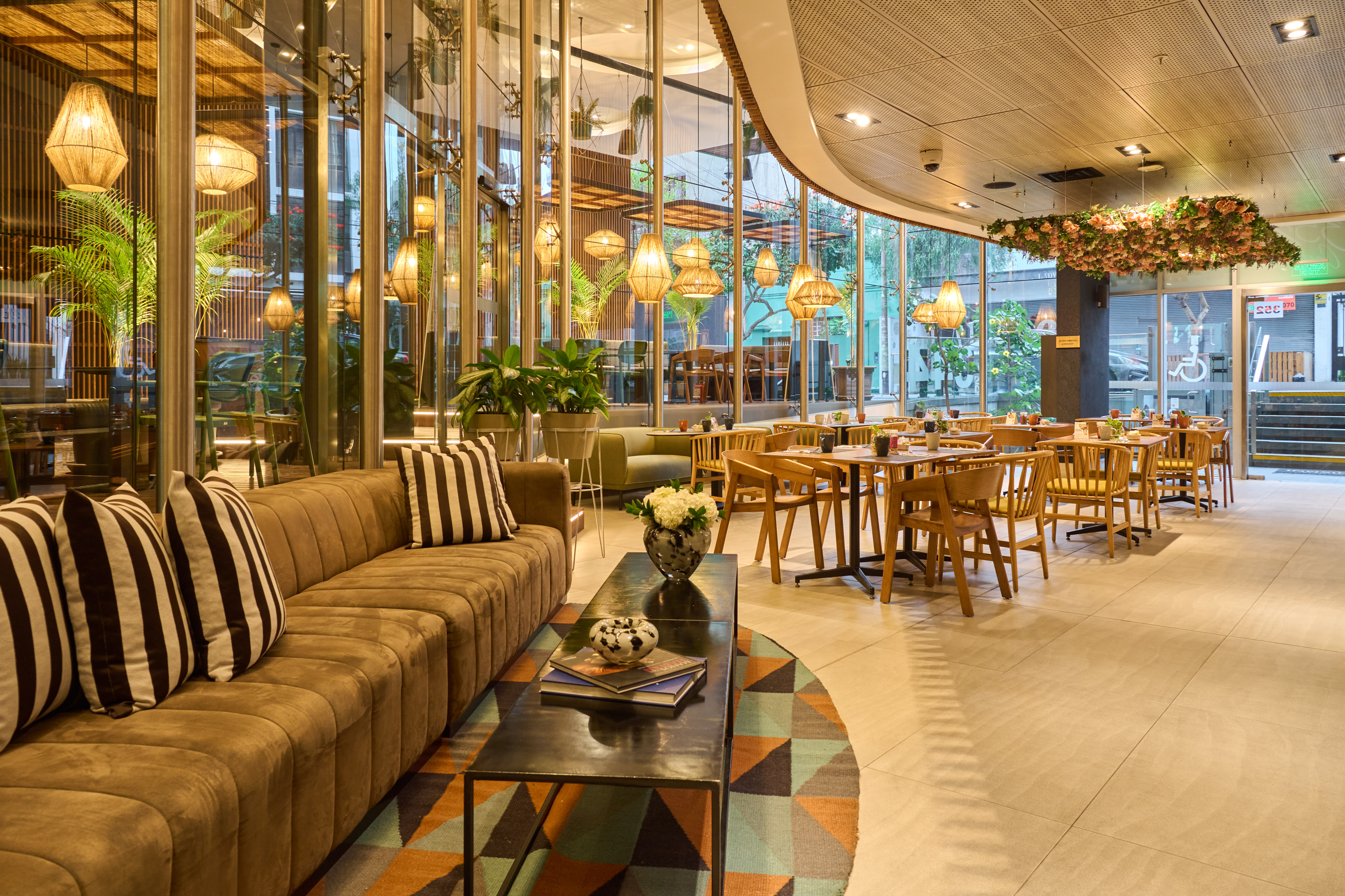 Modern hotel lounge with glass walls, woven pendant lights, and brown sofa.