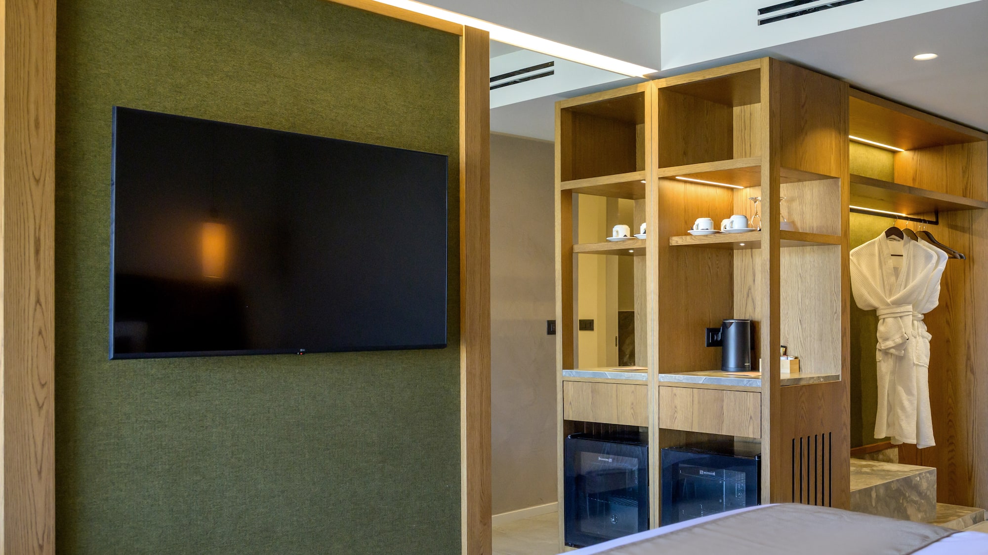 Modern hotel room with green wall, mounted TV, wooden cabinet, and minibar.