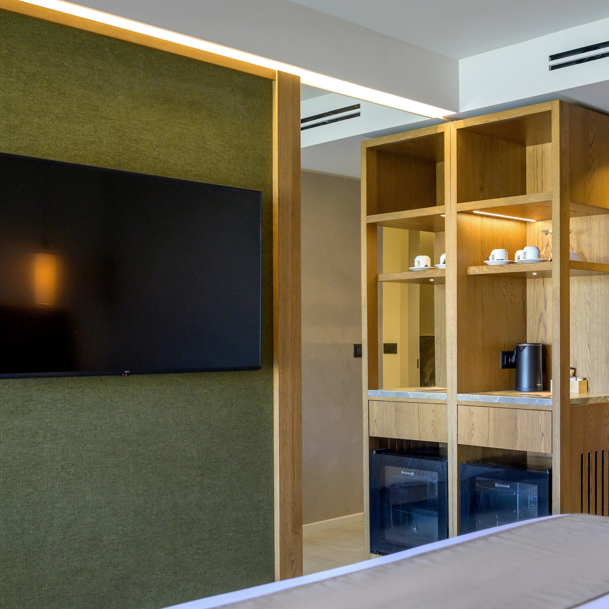 Modern hotel room with green wall, mounted TV, wooden cabinet, and minibar.