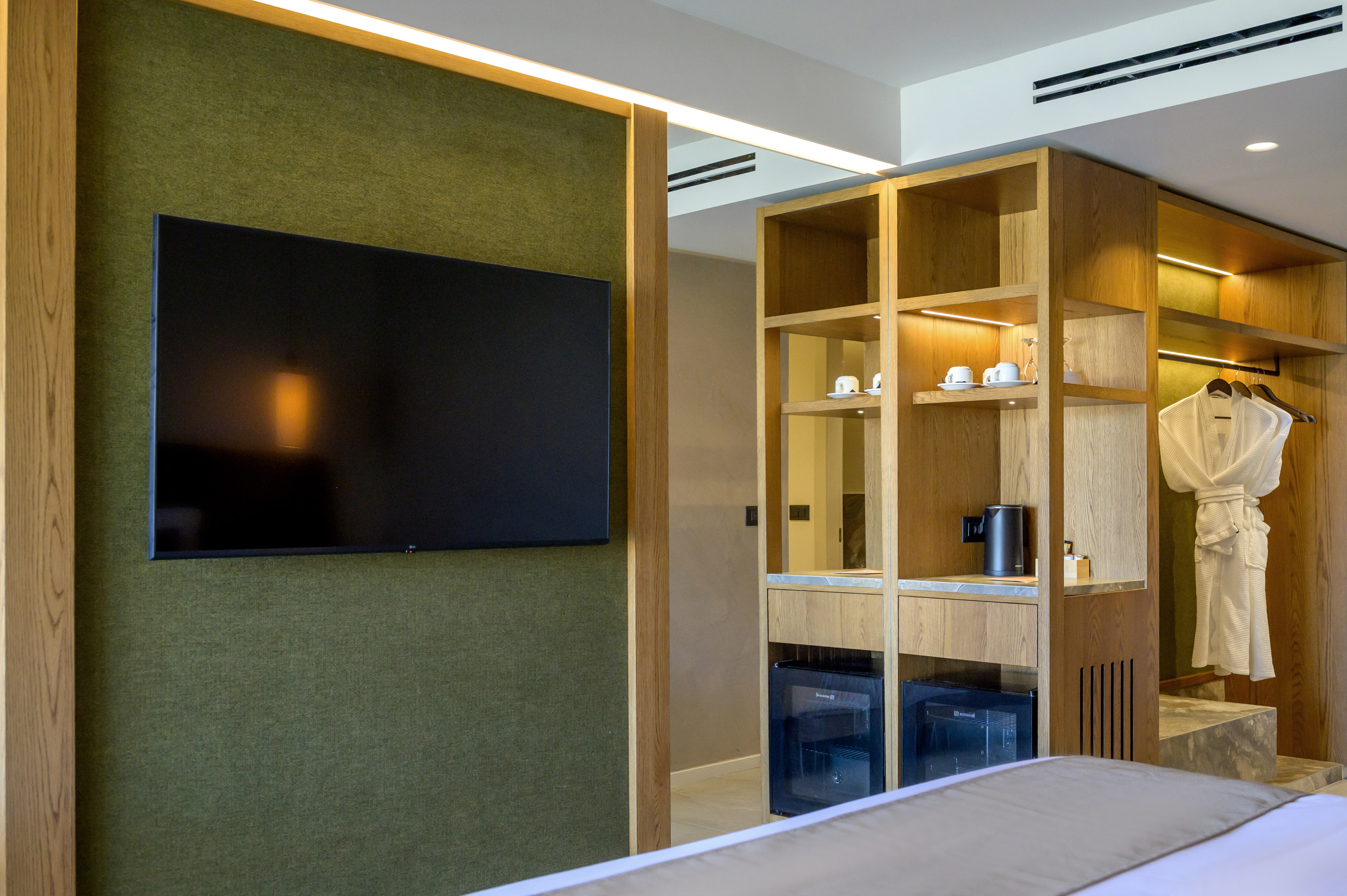 Modern hotel room with green wall, mounted TV, wooden cabinet, and minibar.