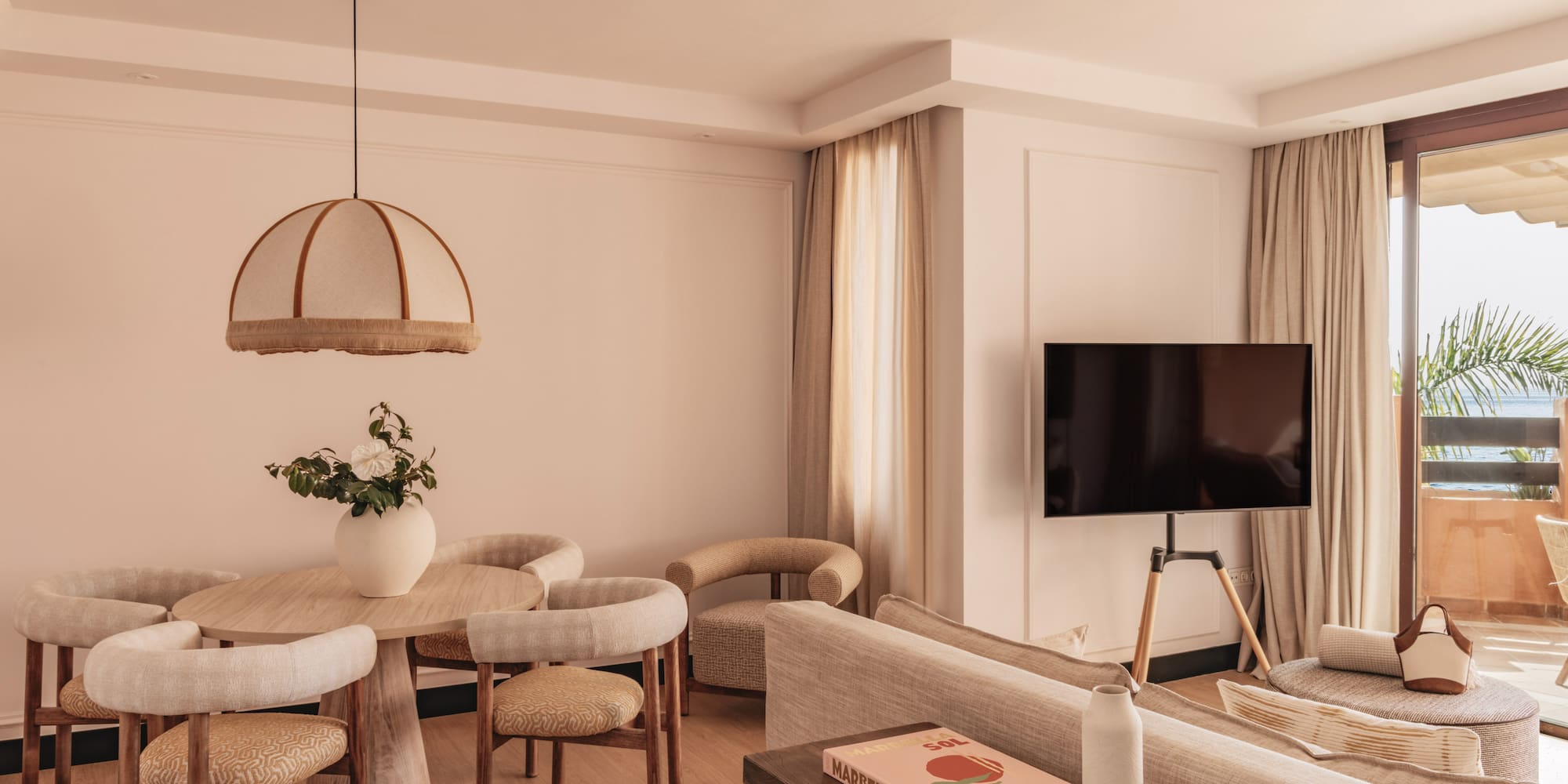 Modern hotel suite living room, dining area, TV, and balcony with sea view.