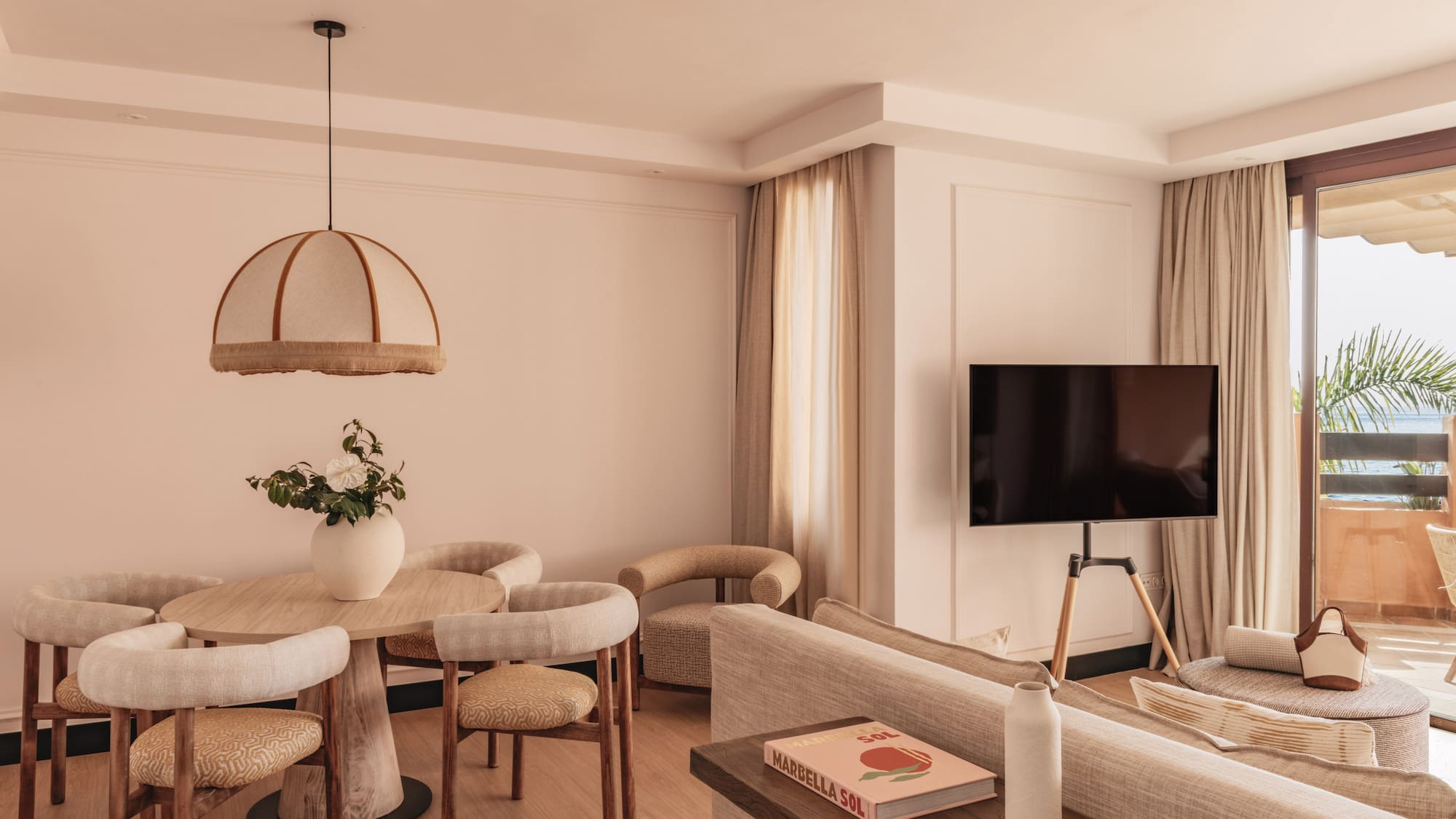 Modern hotel suite living room, dining area, TV, and balcony with sea view.