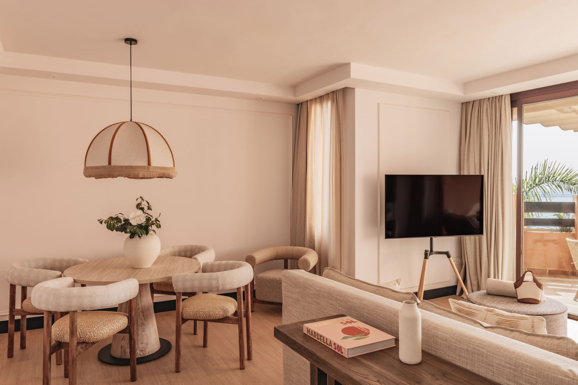 Modern hotel suite living room, dining area, TV, and balcony with sea view.