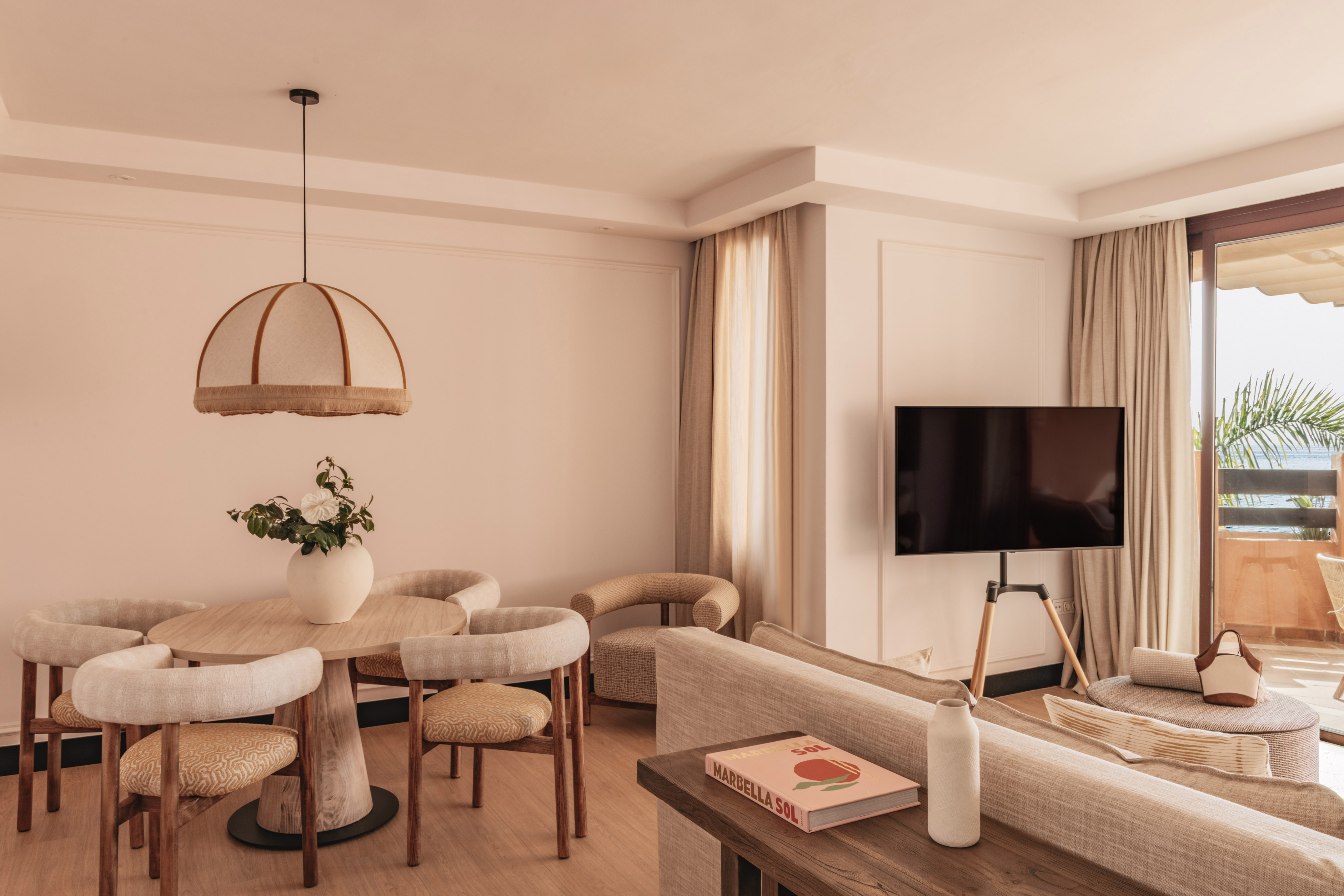 Modern hotel suite living room, dining area, TV, and balcony with sea view.