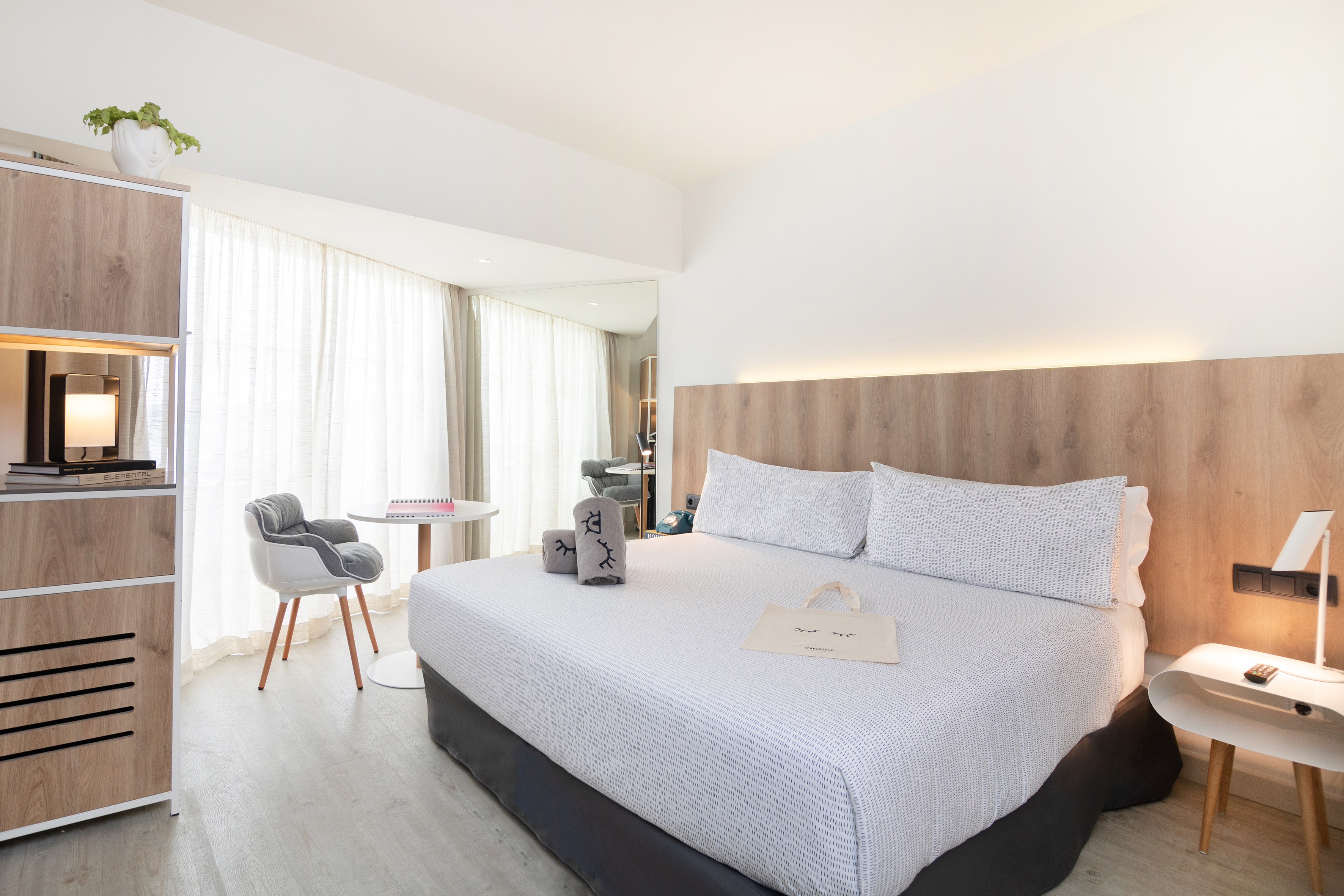 Modern hotel room with large white bed, wood accents, and bright natural light.