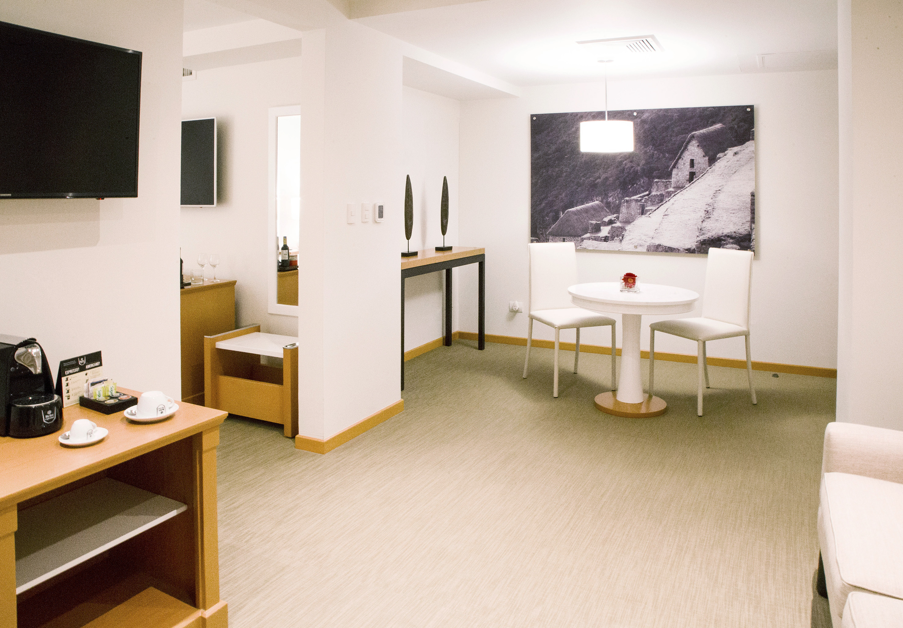 Hotel suite living area with dining table, coffee machine, and large artwork.