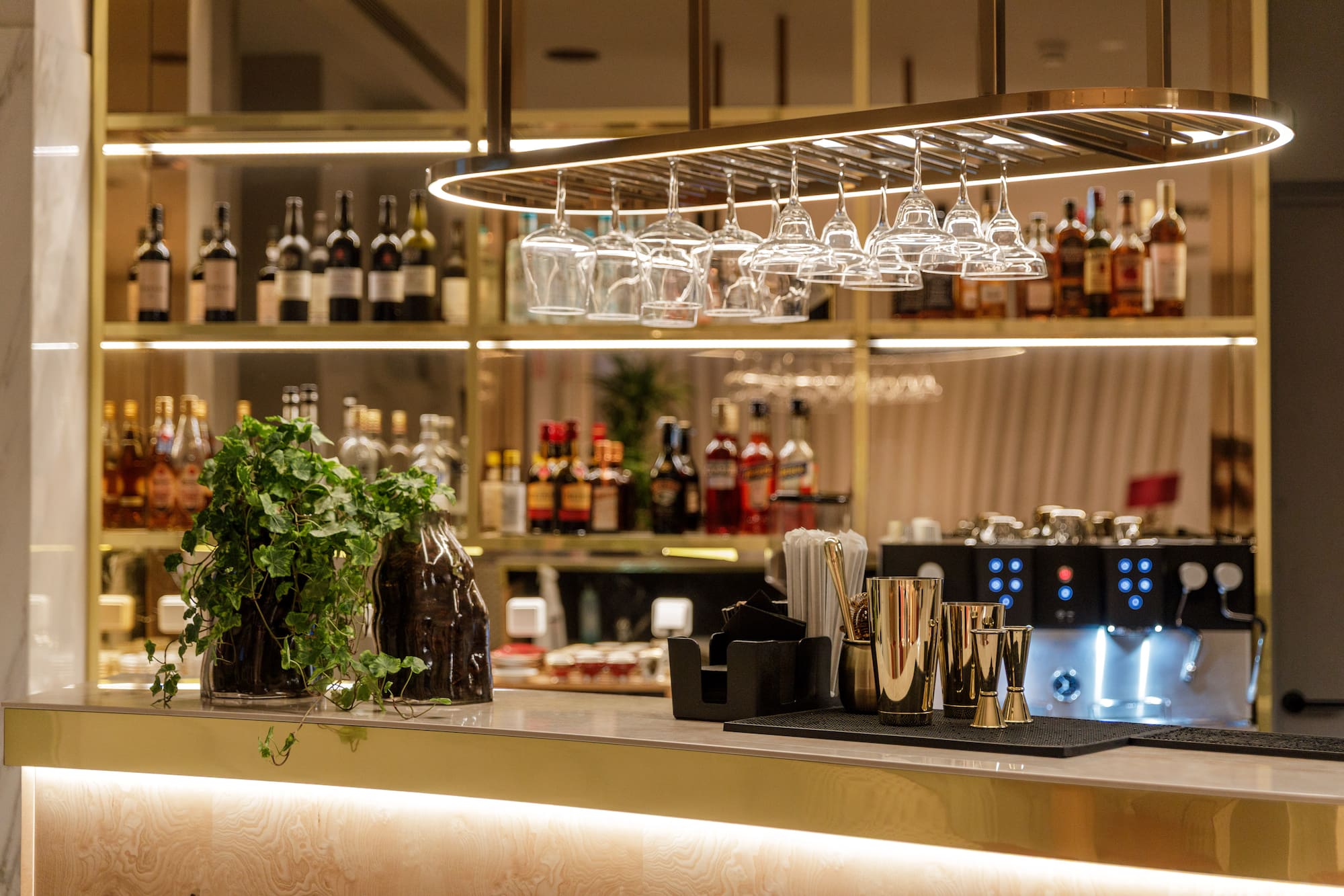 Modern bar with gold accents, liquor bottles, hanging glasses, and bar tools.