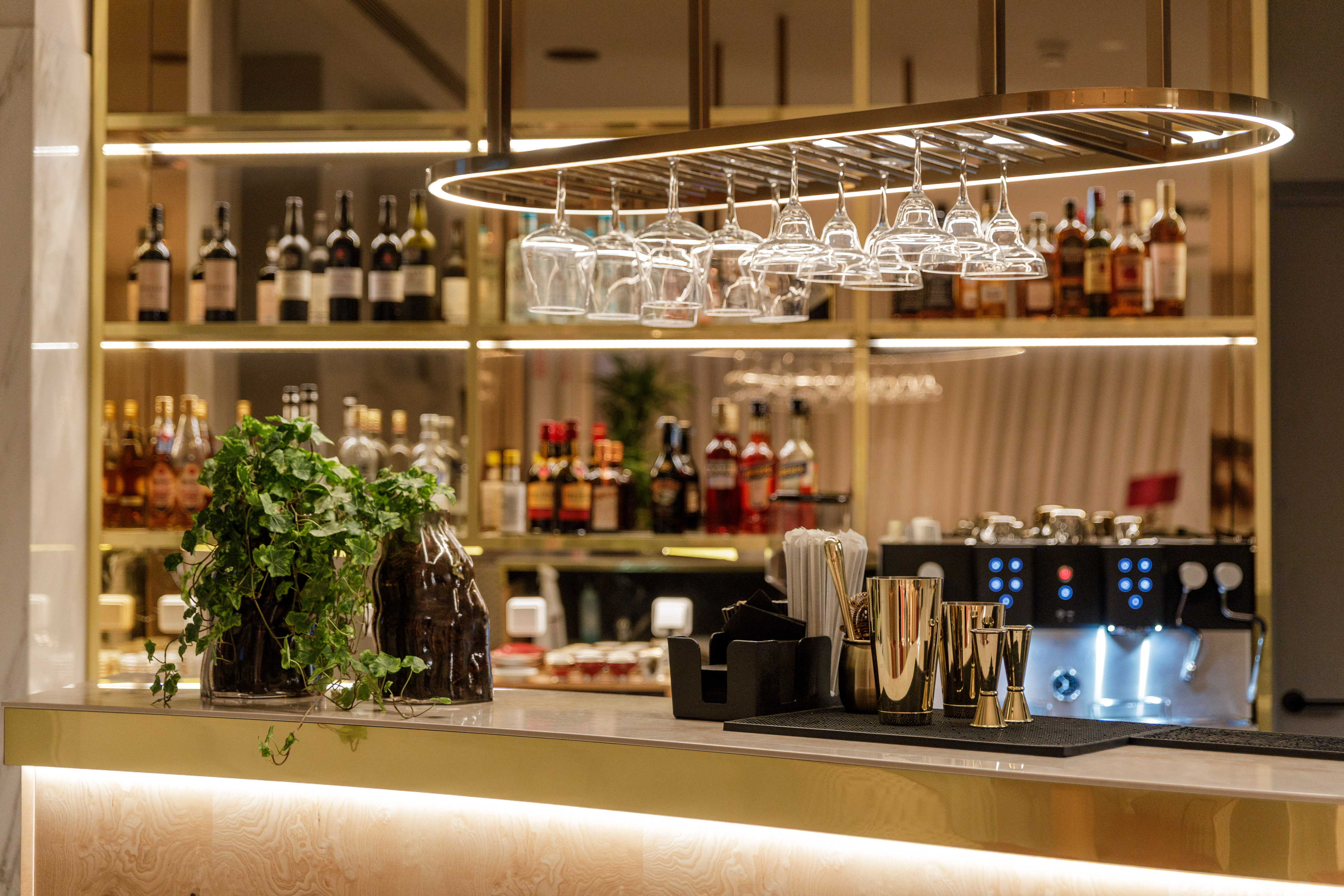 Modern bar with gold accents, liquor bottles, hanging glasses, and bar tools.