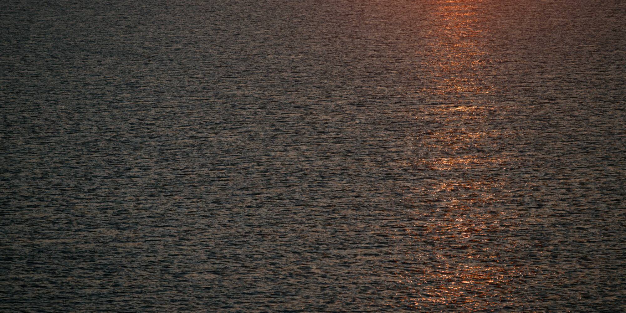 Ondas de agua oscura con reflejo naranja del atardecer.