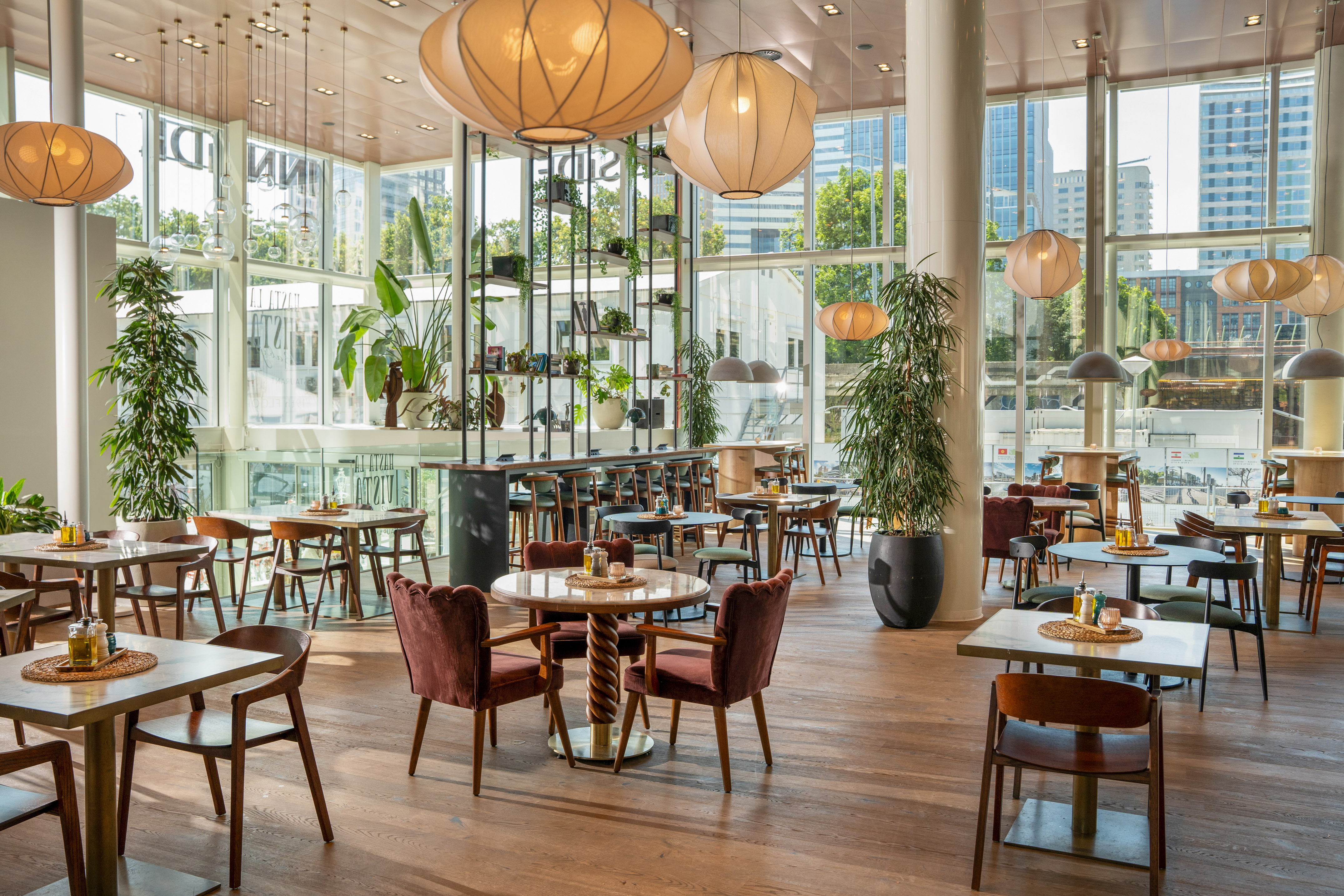 Bright, modern restaurant interior with dining tables, potted plants, and large windows.