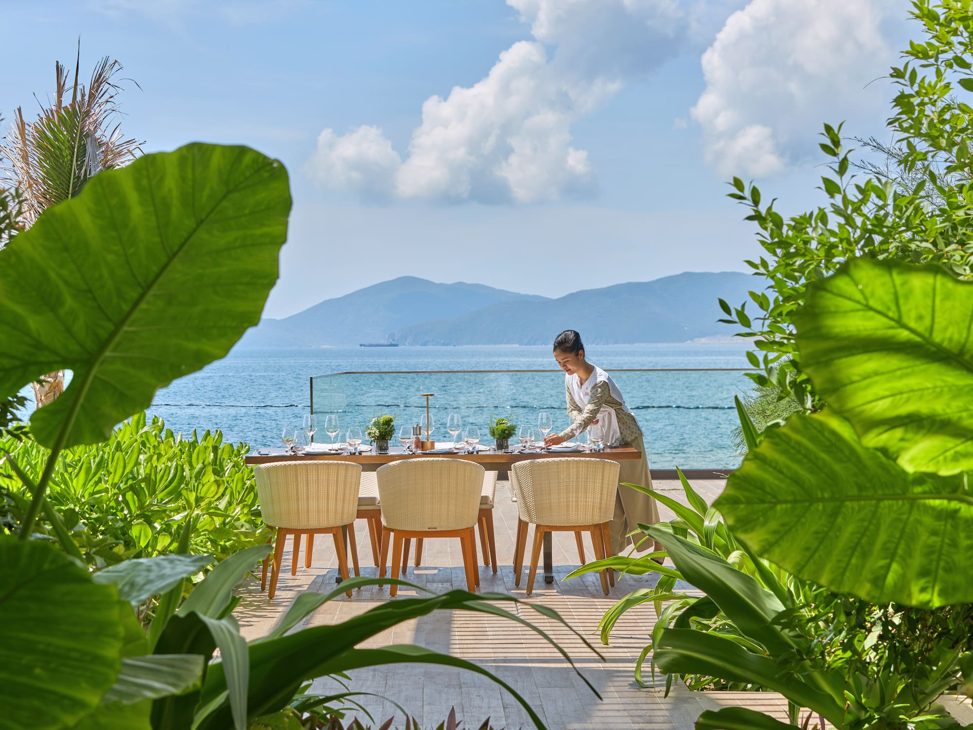 a woman sitting at a table with chairs and a view of the ocean