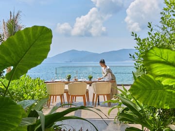 a woman sitting at a table with chairs and a view of the ocean