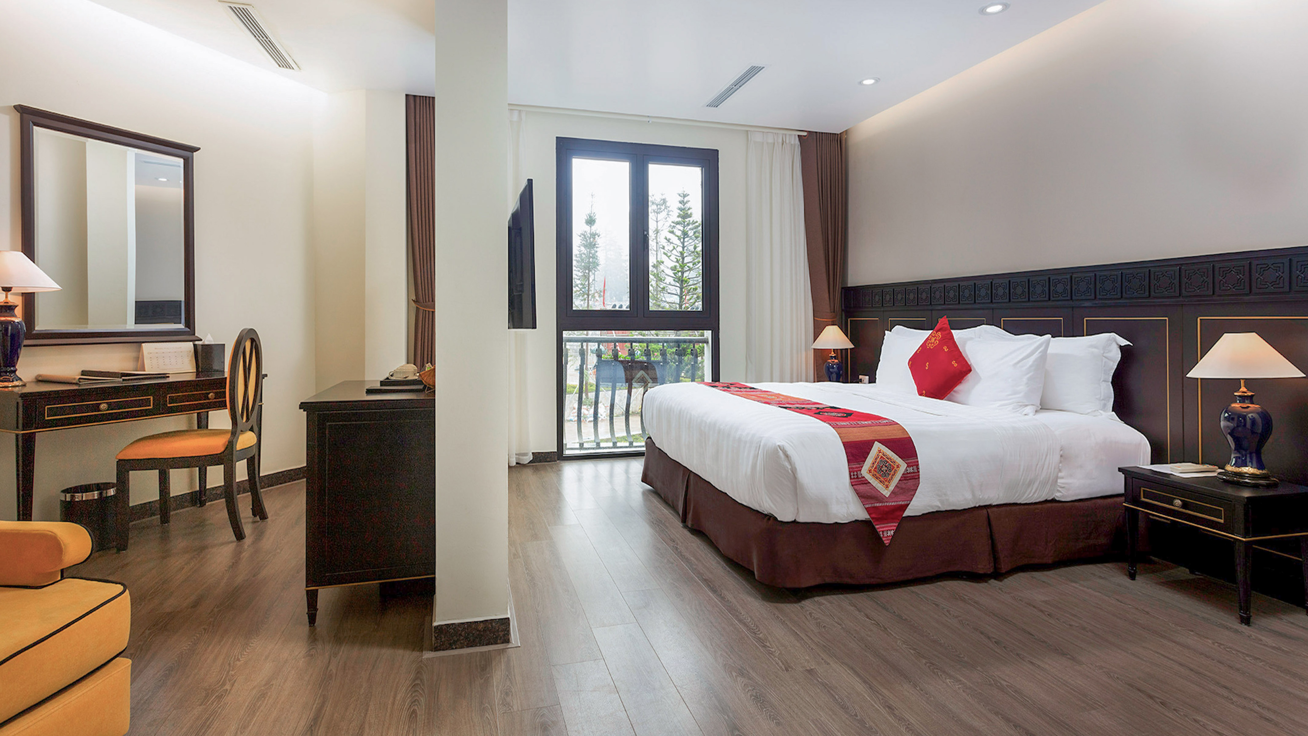 Elegant hotel bedroom with large bed, patterned runner, desk, and balcony.