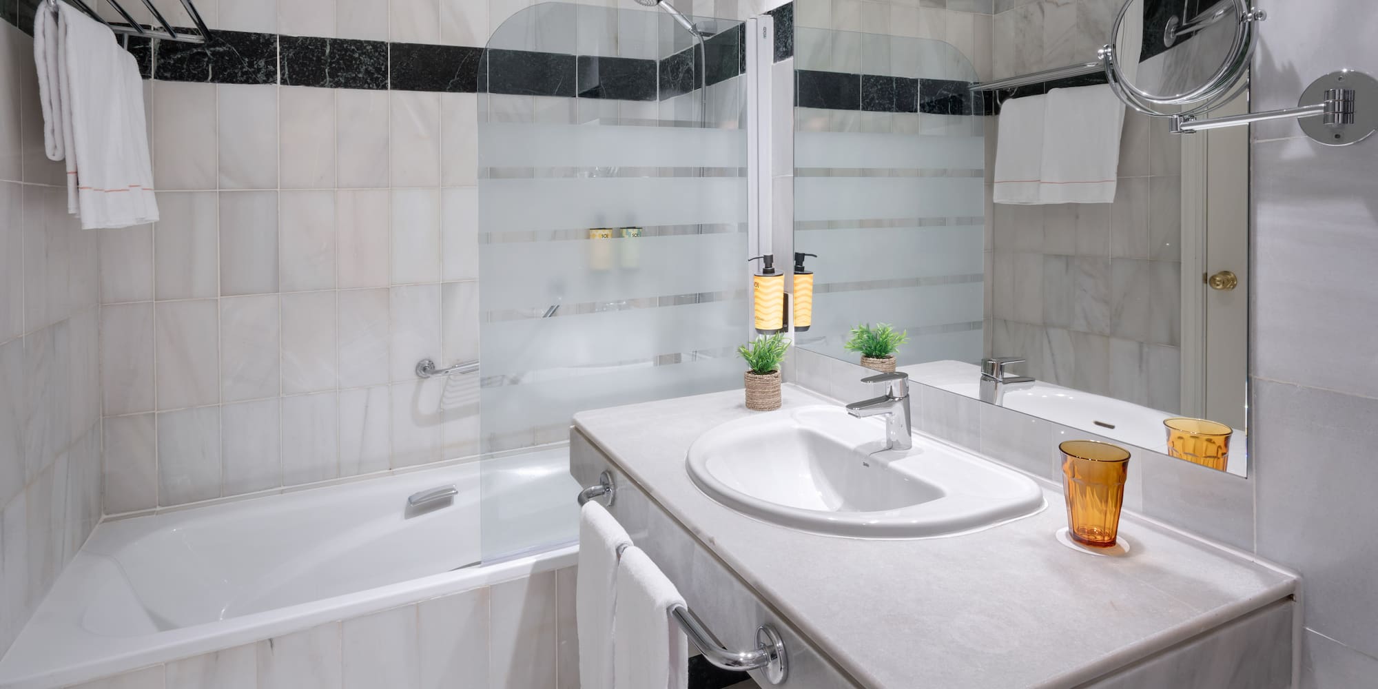 Baño moderno de hotel con bañera, lavabo de mármol, ducha y toallas.