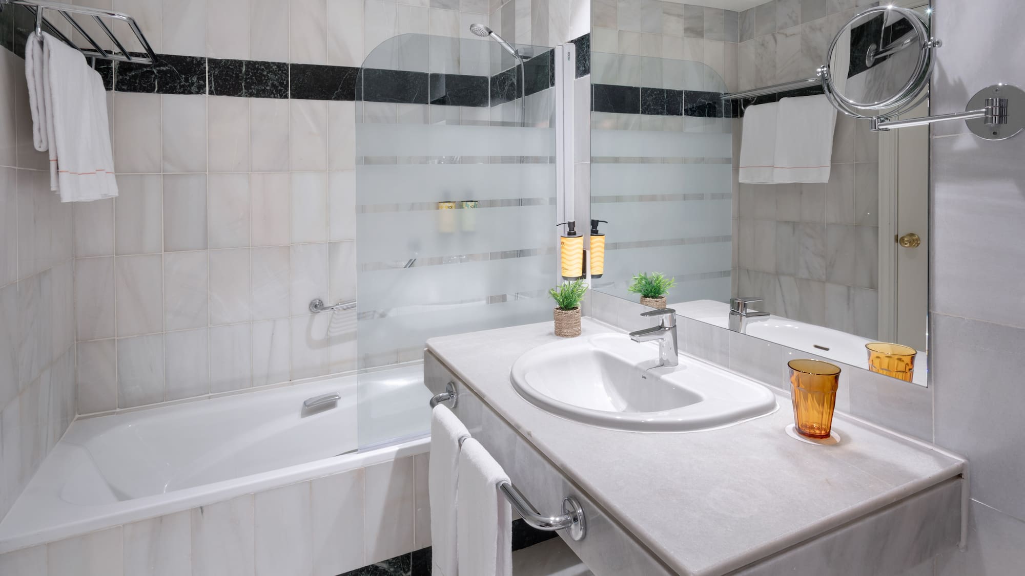 Baño moderno de hotel con bañera, lavabo de mármol, ducha y toallas.