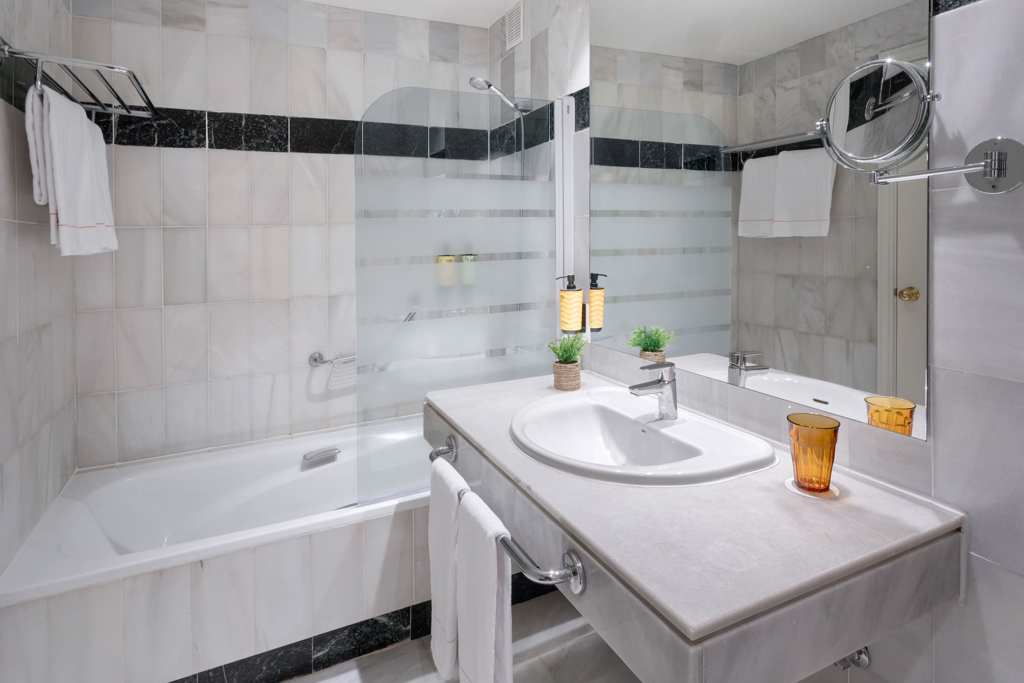 Baño moderno de hotel con bañera, lavabo de mármol, ducha y toallas.