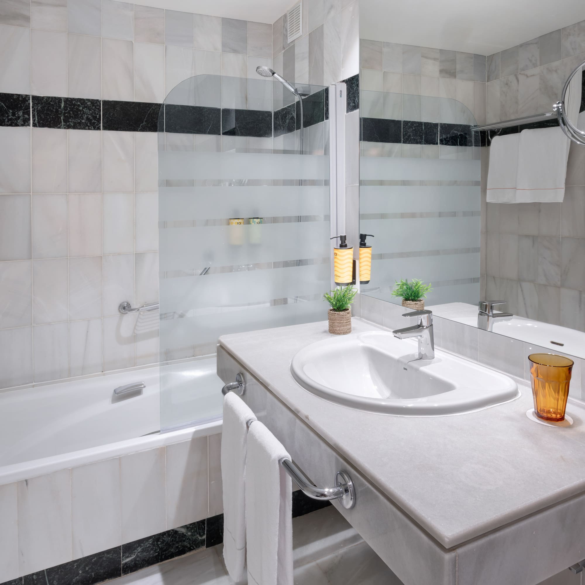 White marble hotel bathroom with bathtub, shower, vanity sink, and mirror.